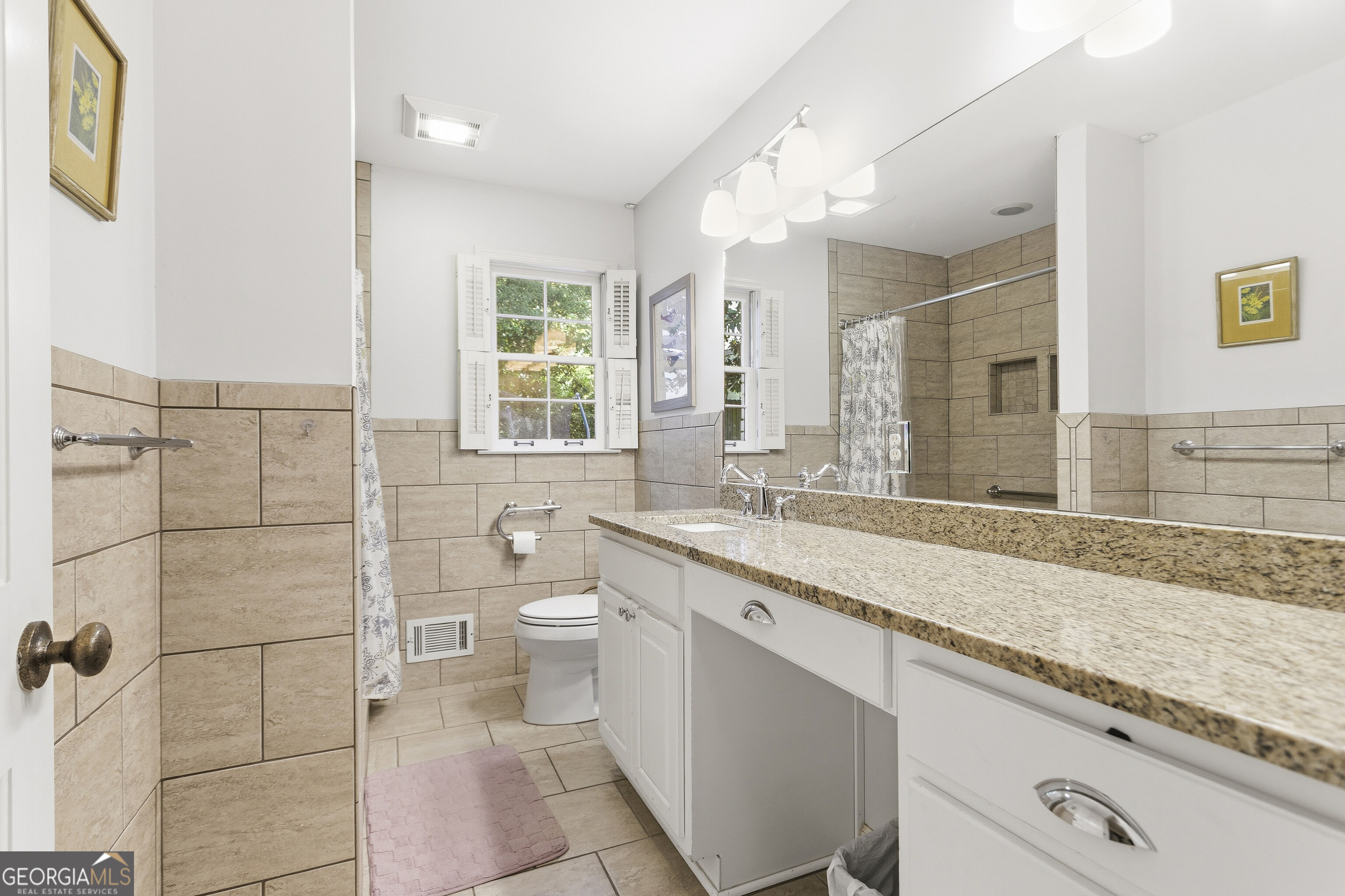 Bathroom with a long granite vanity, large mirror, and beige tiled shower and walls.