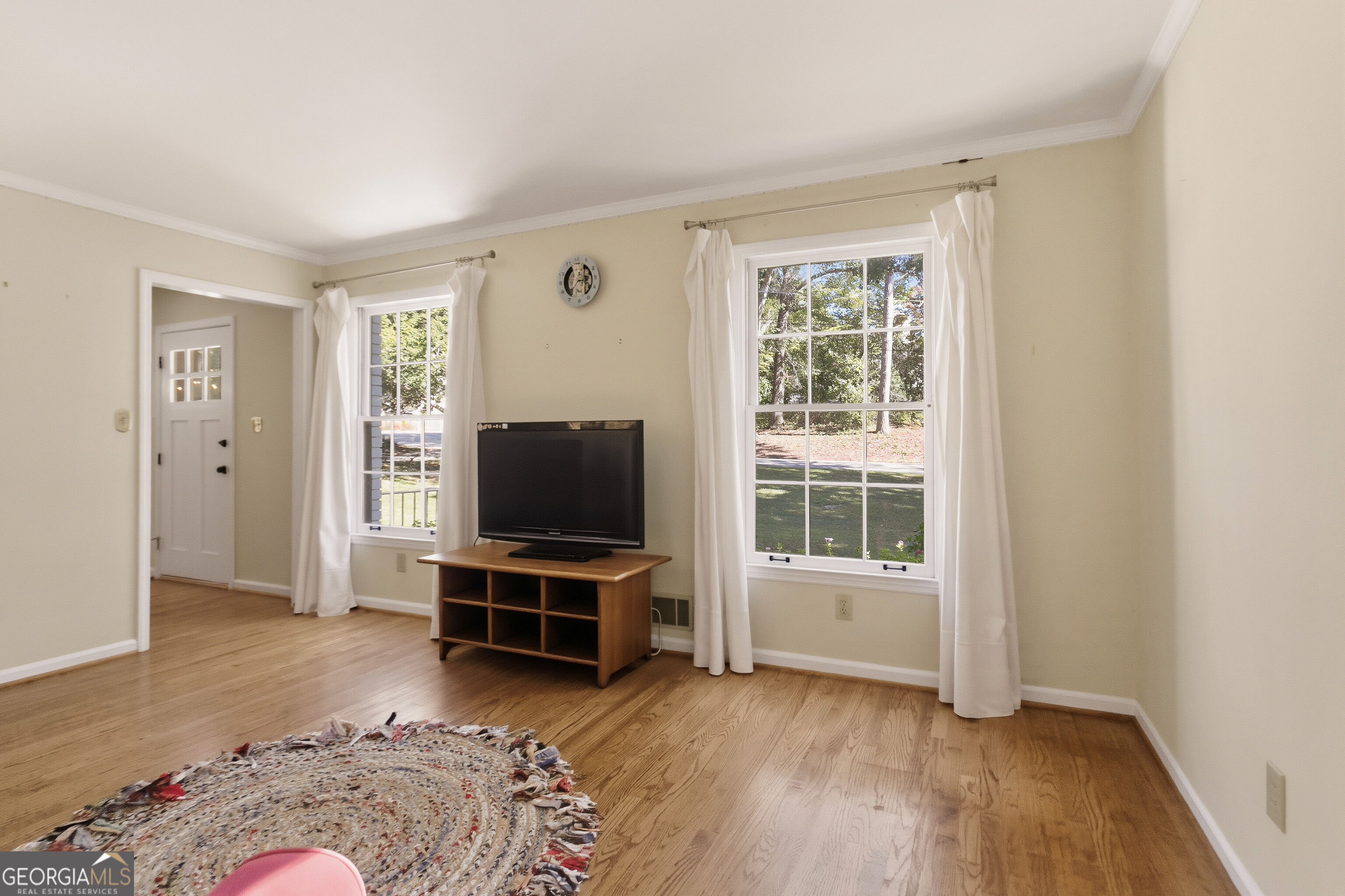 Living room with hardwood floors, curtained windows, and a television on a wooden stand.