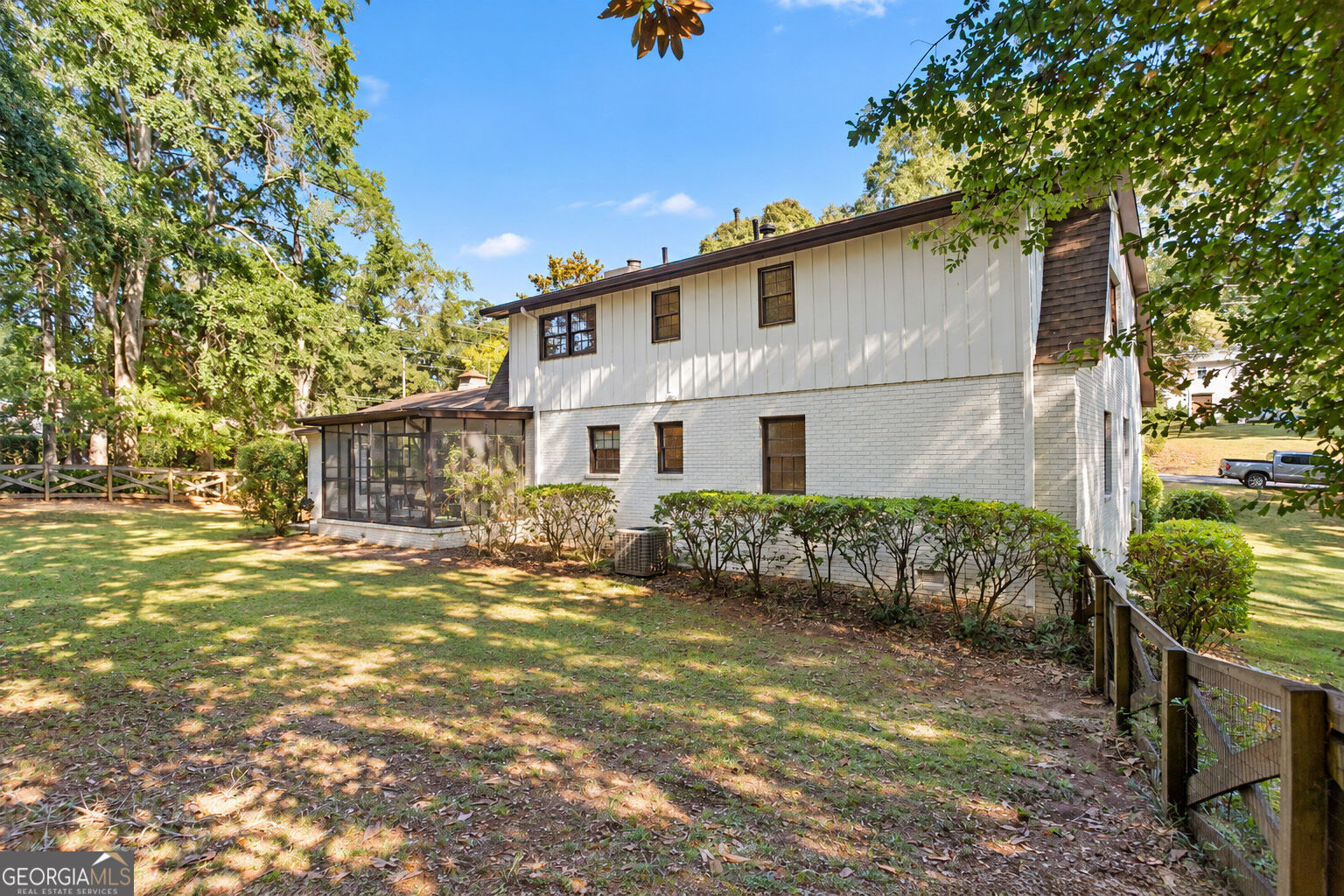 Two-story white house with a screened porch beside a shaded, fenced lawn.