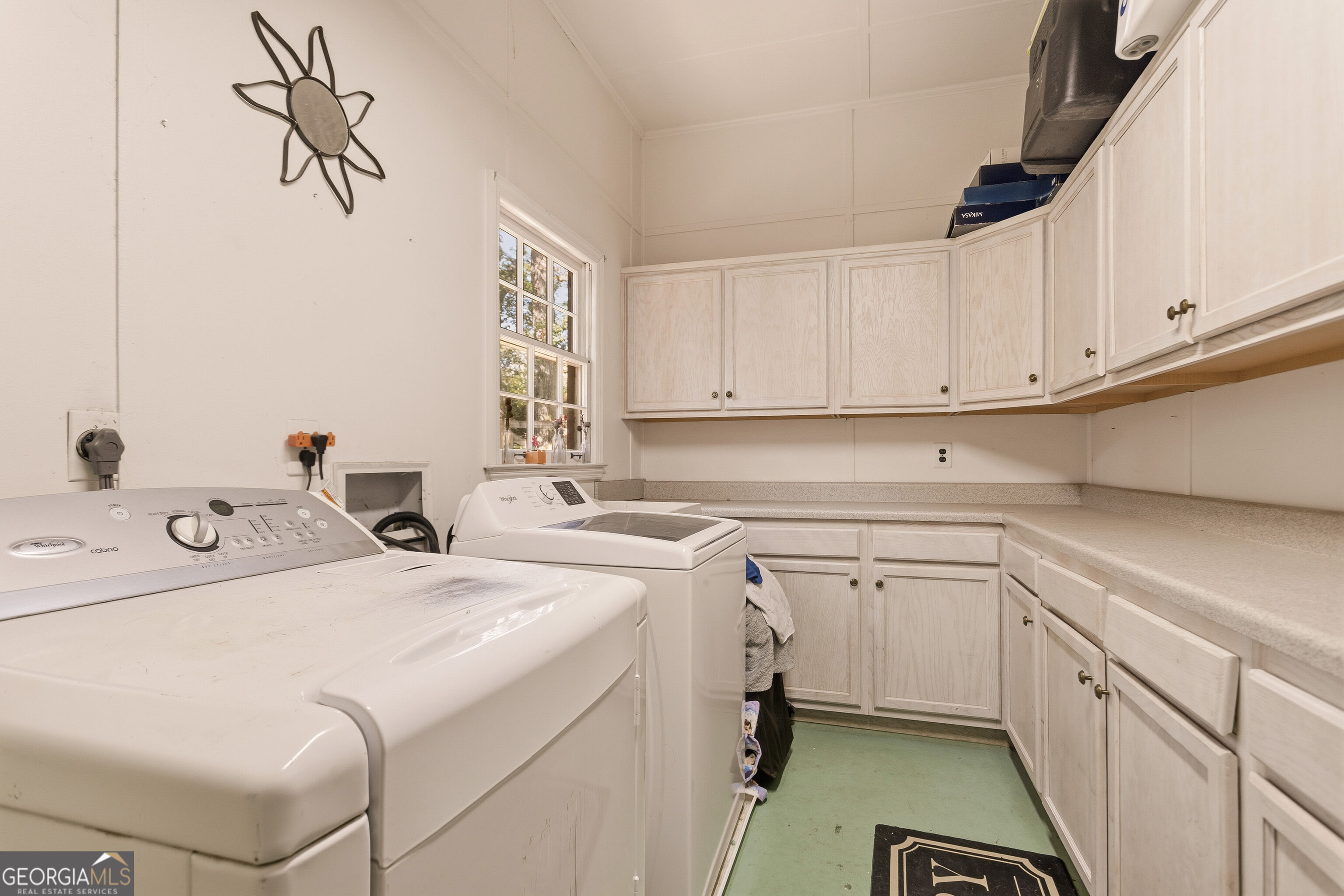 Laundry room with two top-loading washers, extensive light wood cabinetry, and a long countertop.