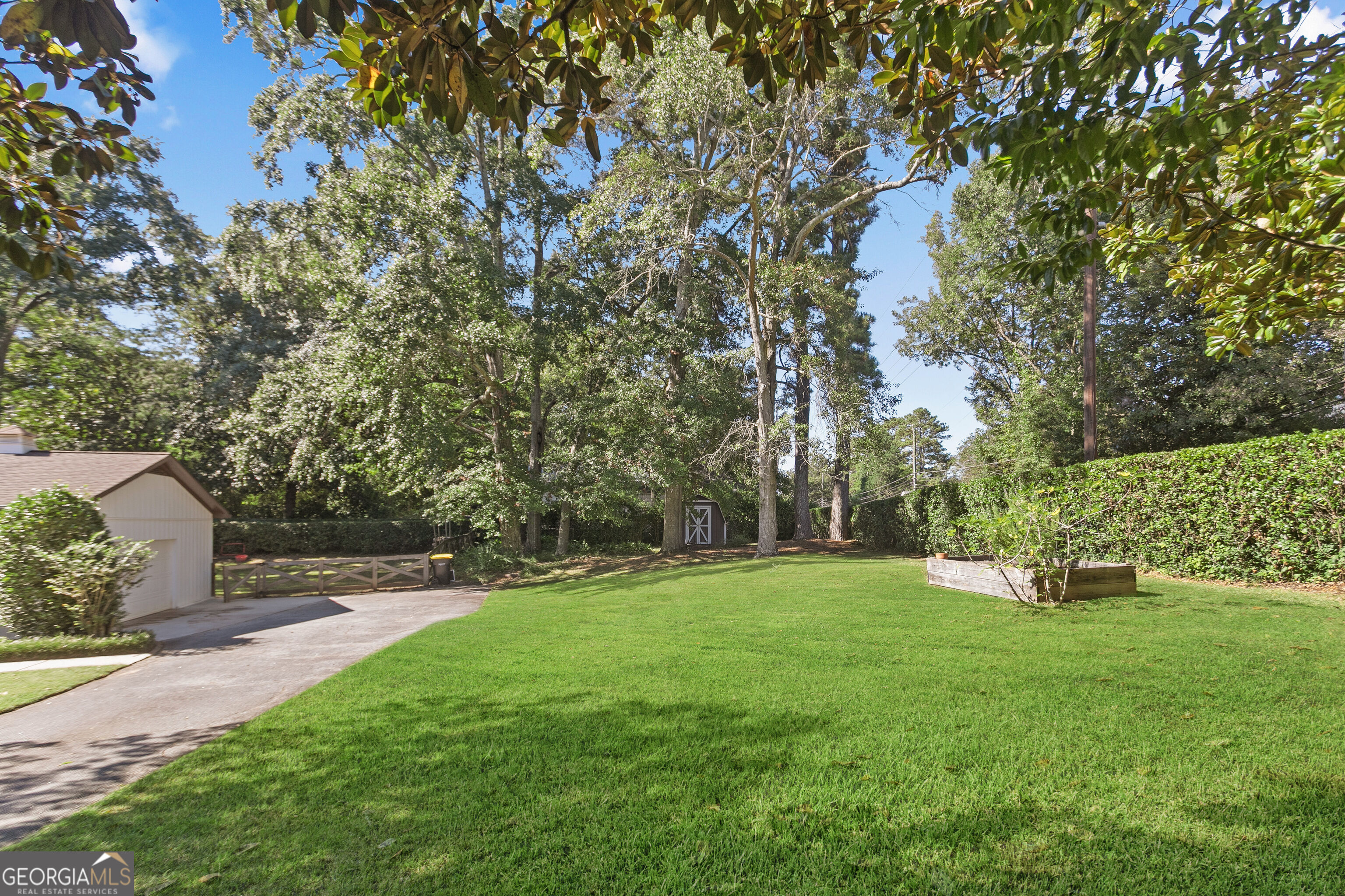 Backyard with a broad lawn, mature trees, raised garden bed, and small shed.