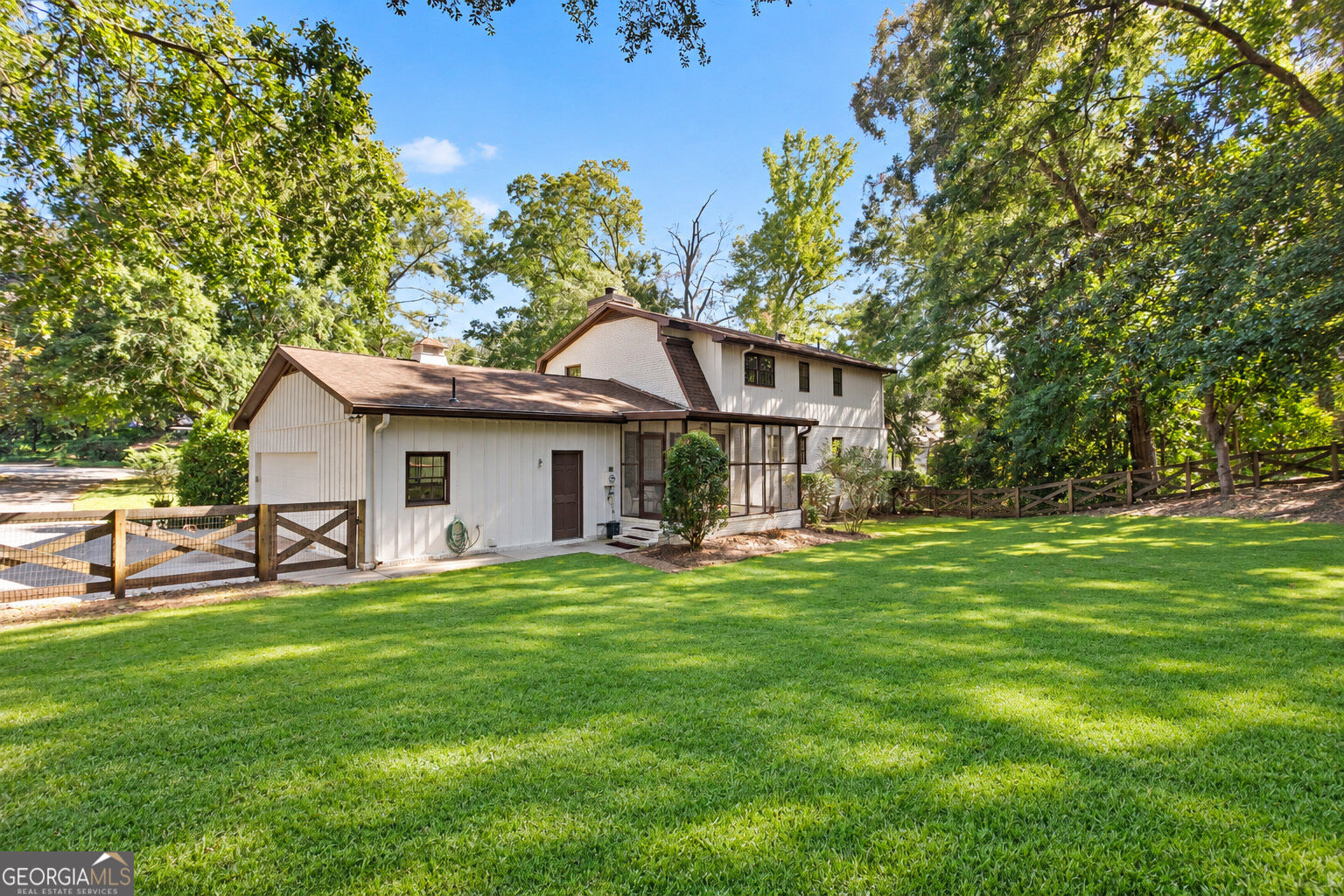 White two-story home with a screened porch, fenced lawn, and mature trees.