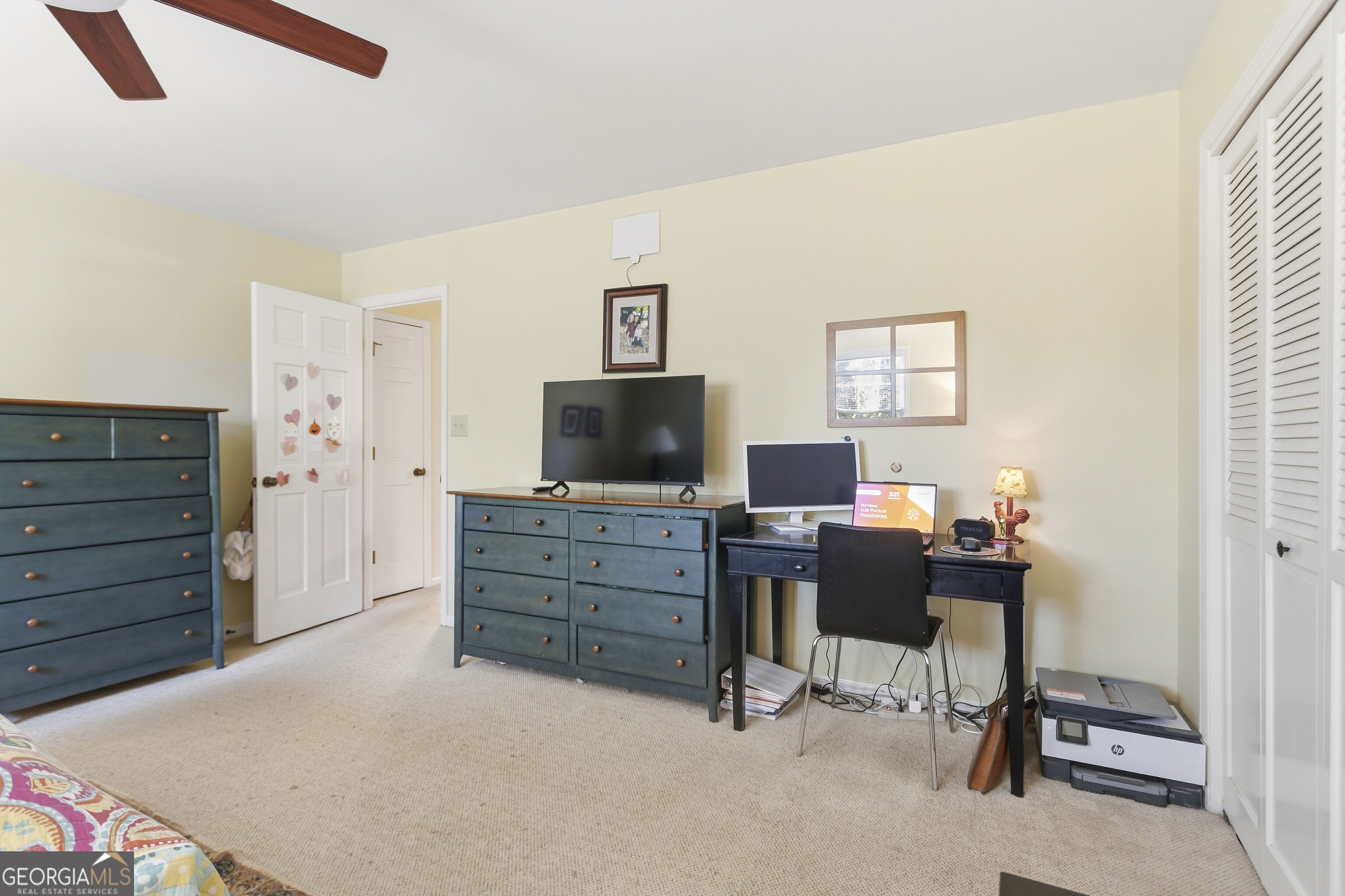 Furnished bedroom with blue-green dressers, a desk and computer, and white louvered closet doors.