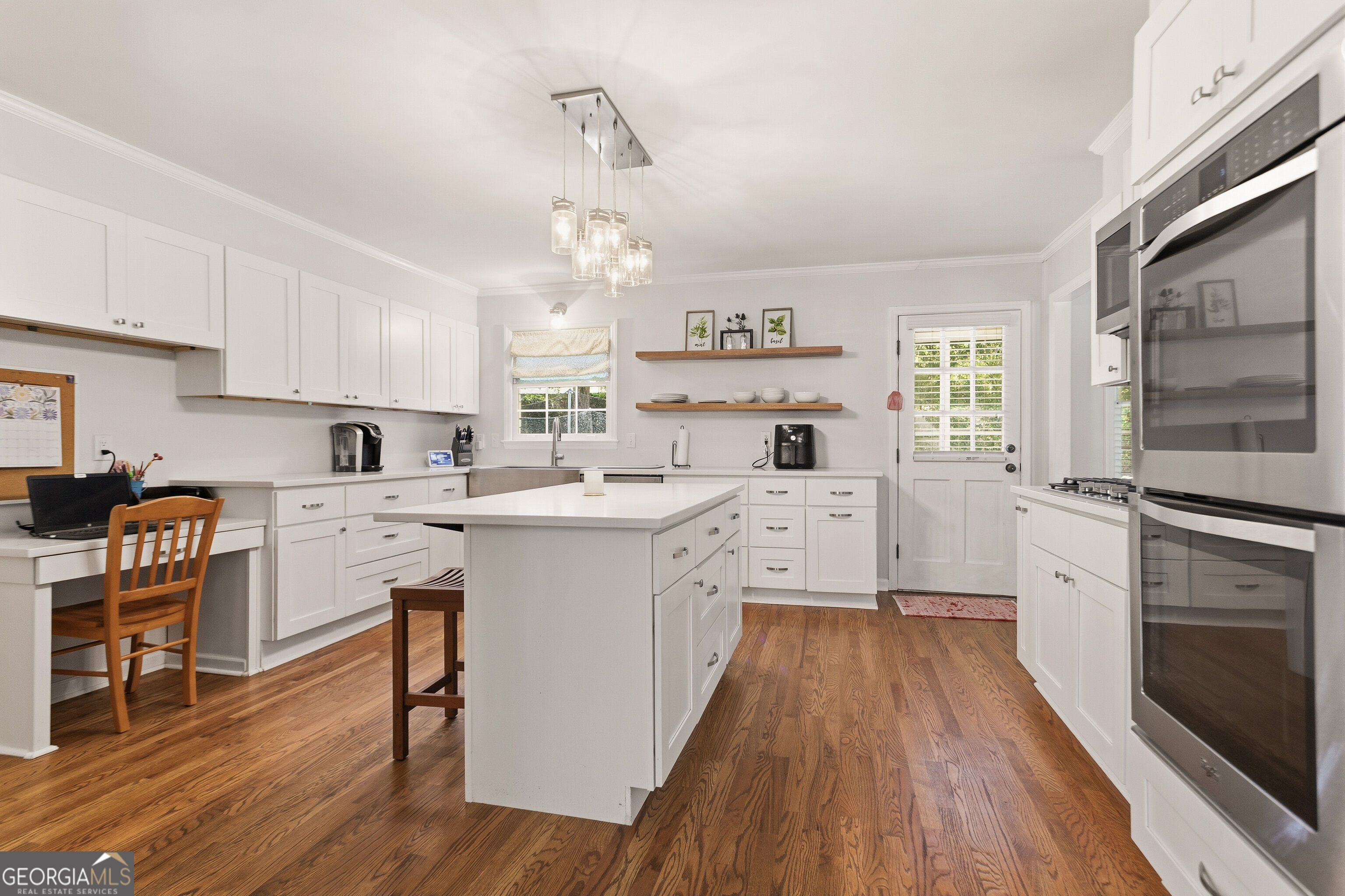 Bright white kitchen with a large island, hardwood floors, stainless steel appliances, and a built-in desk.