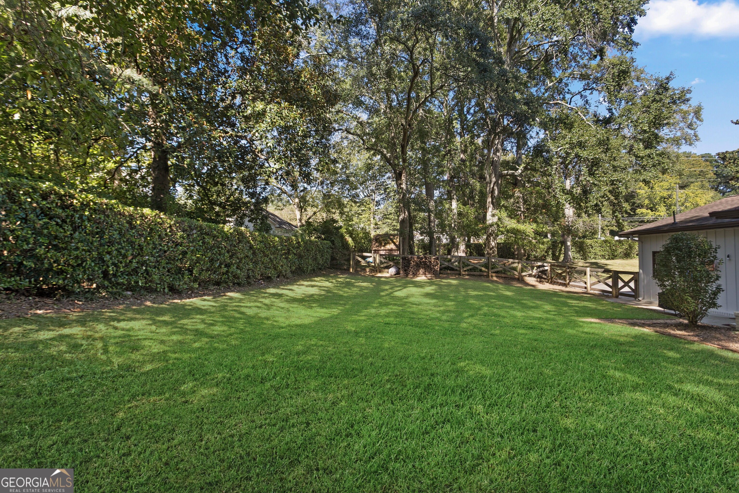 Spacious backyard with a broad lawn, mature shade trees, and a wooden fence.