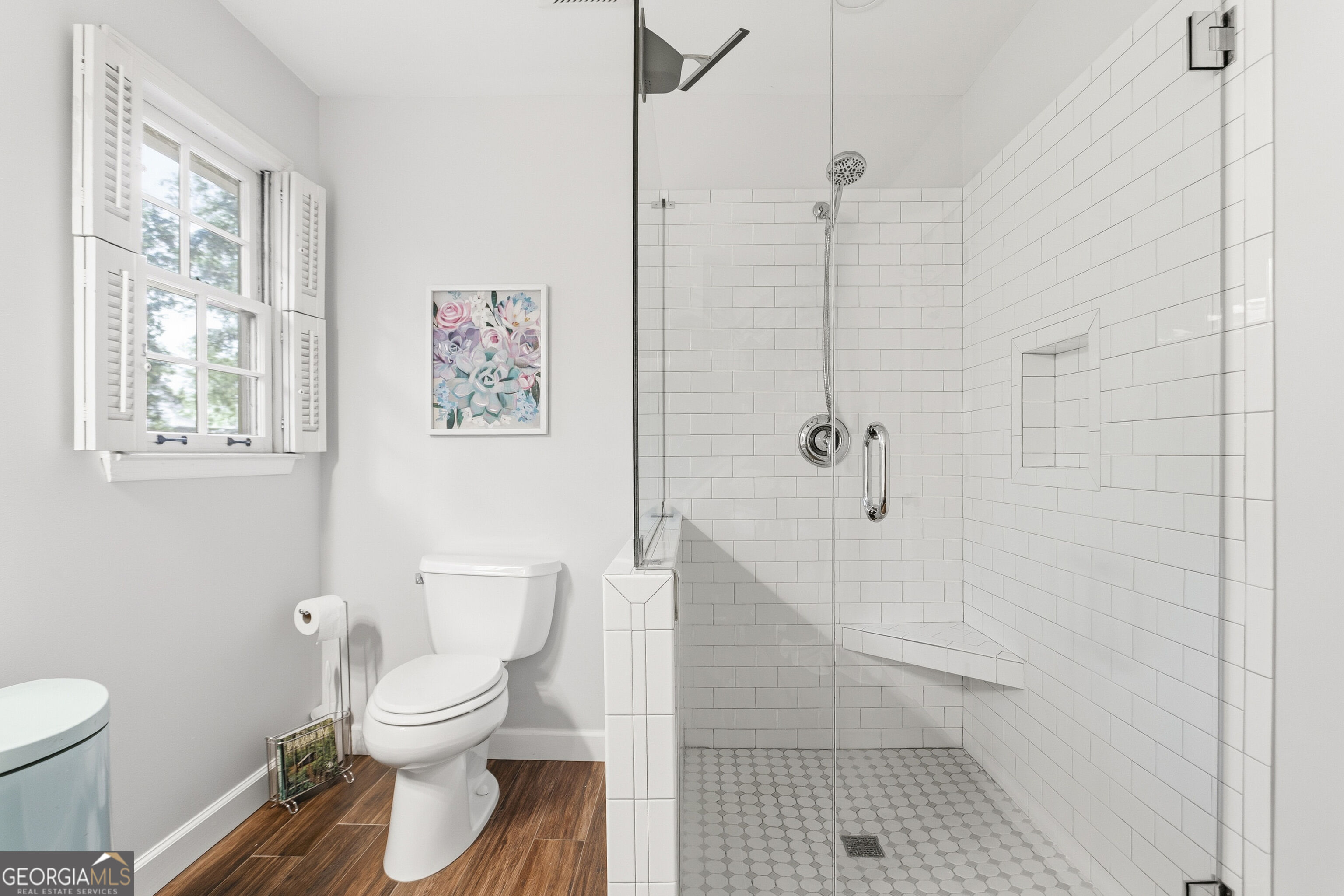 Bathroom with a white-tiled walk-in shower, built-in bench, and shuttered window.