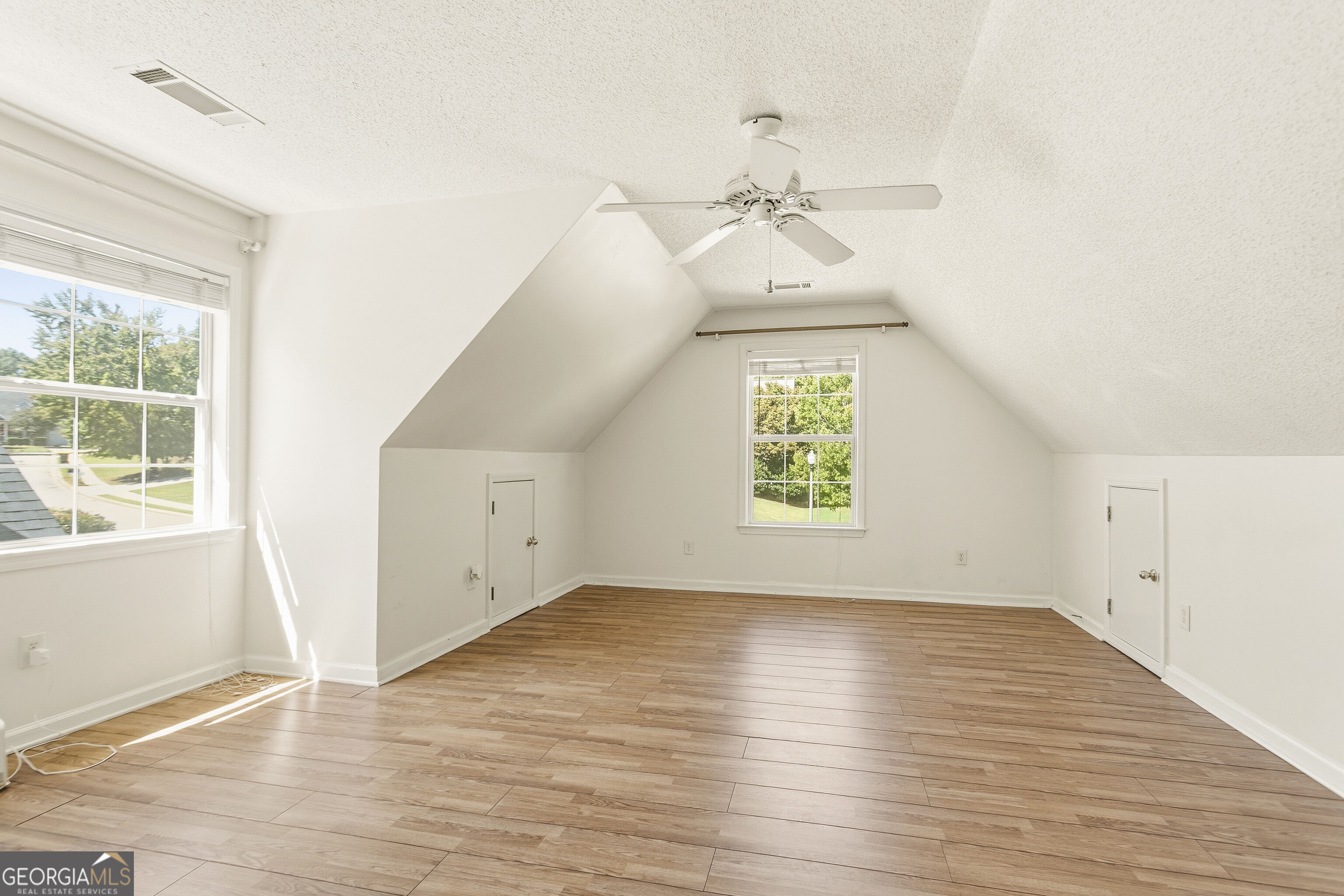Vacant attic room with sloped ceiling, ceiling fan, and wood-look flooring.