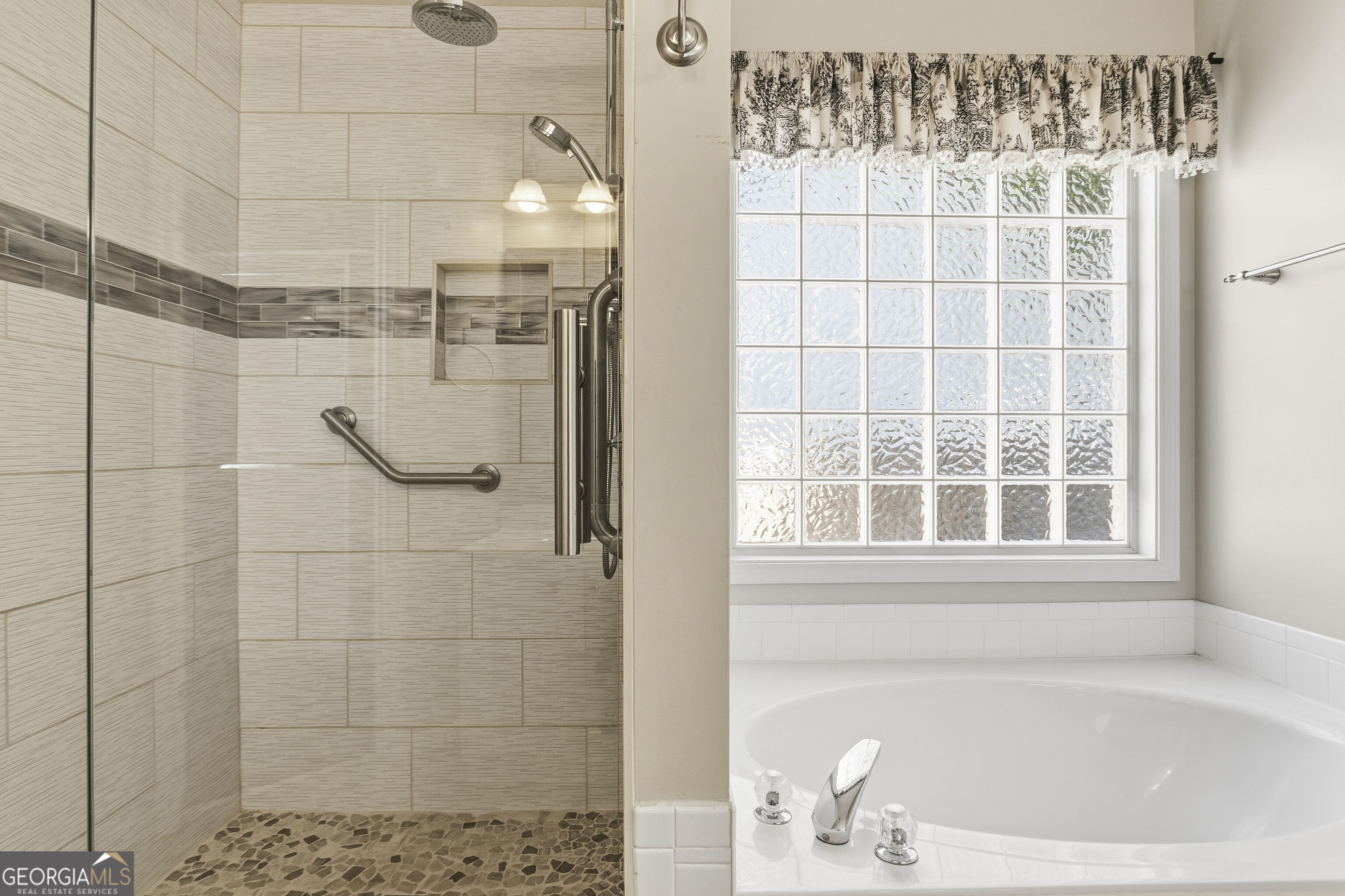 Bathroom with a tiled walk-in shower and grab bars beside a soaking tub and glass-block window.