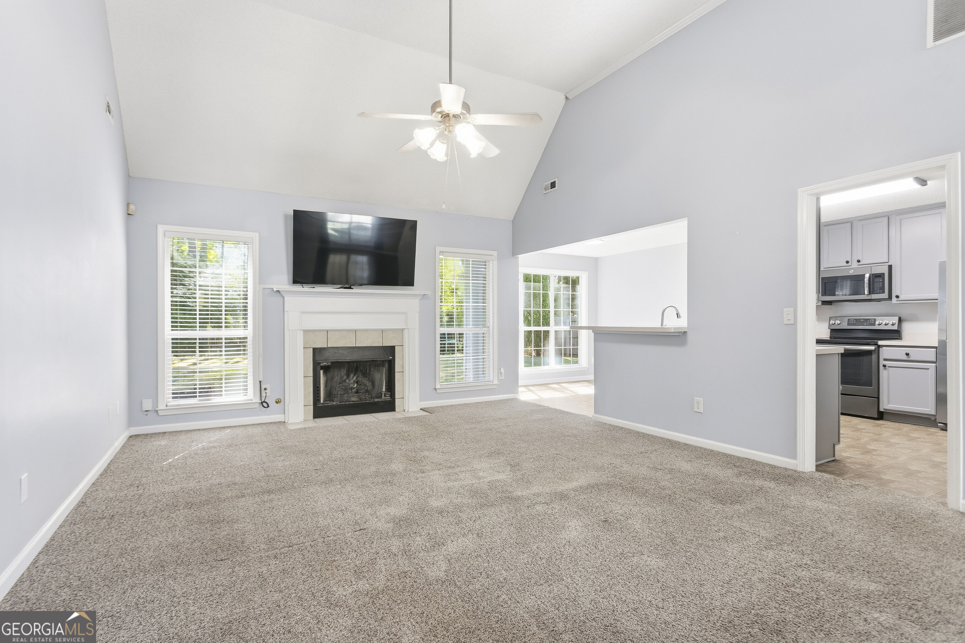 Living room with vaulted ceiling, carpet, and fireplace beneath a mounted television.