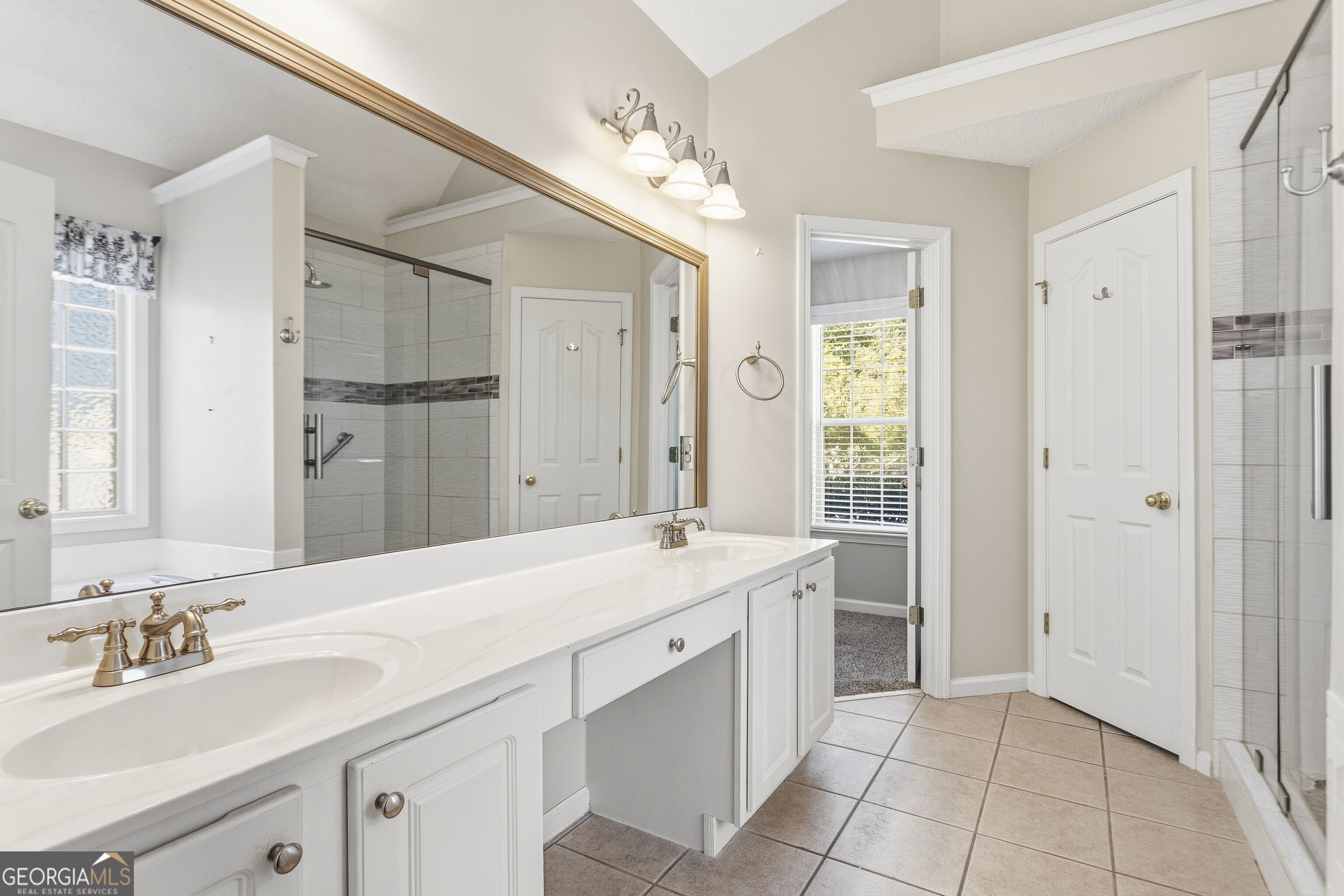 Bathroom with a long white double-sink vanity, brass-tone faucets, and a glass-enclosed tiled shower.