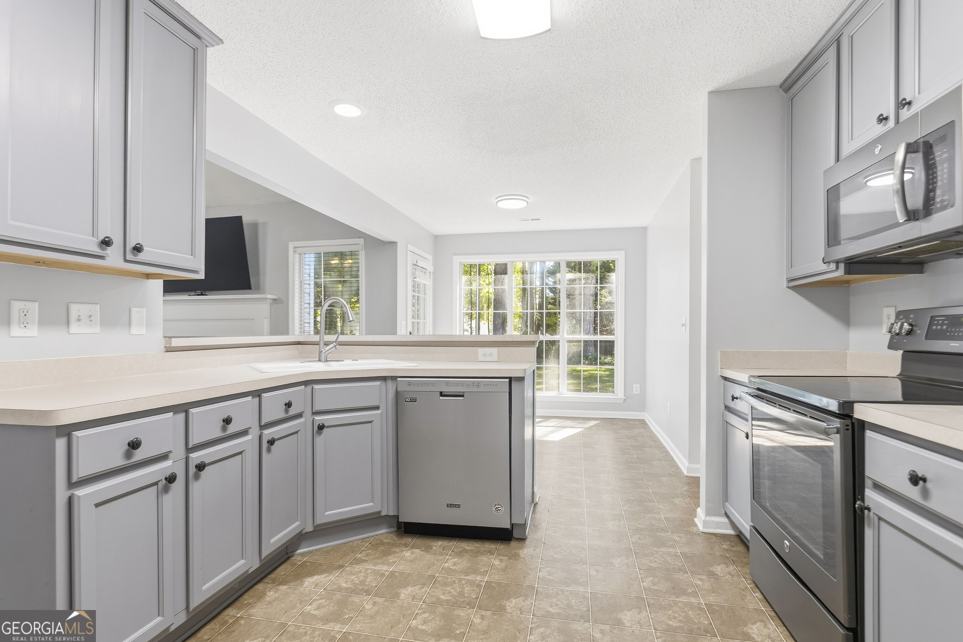 Kitchen with gray cabinets, stainless steel appliances, and a large window overlooking a lawn.