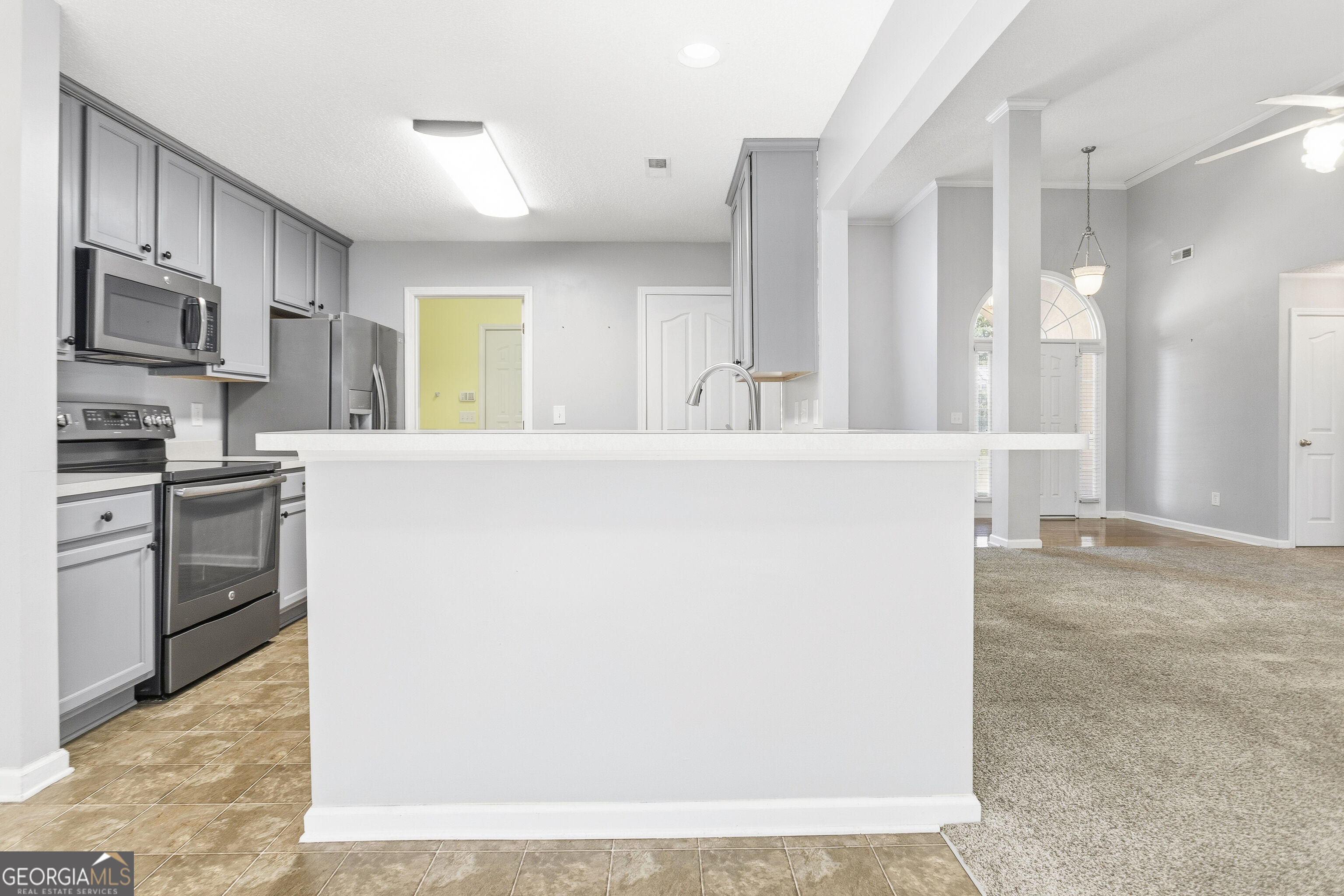 Open kitchen with gray cabinets, stainless appliances, and a large white island beside a carpeted living area.