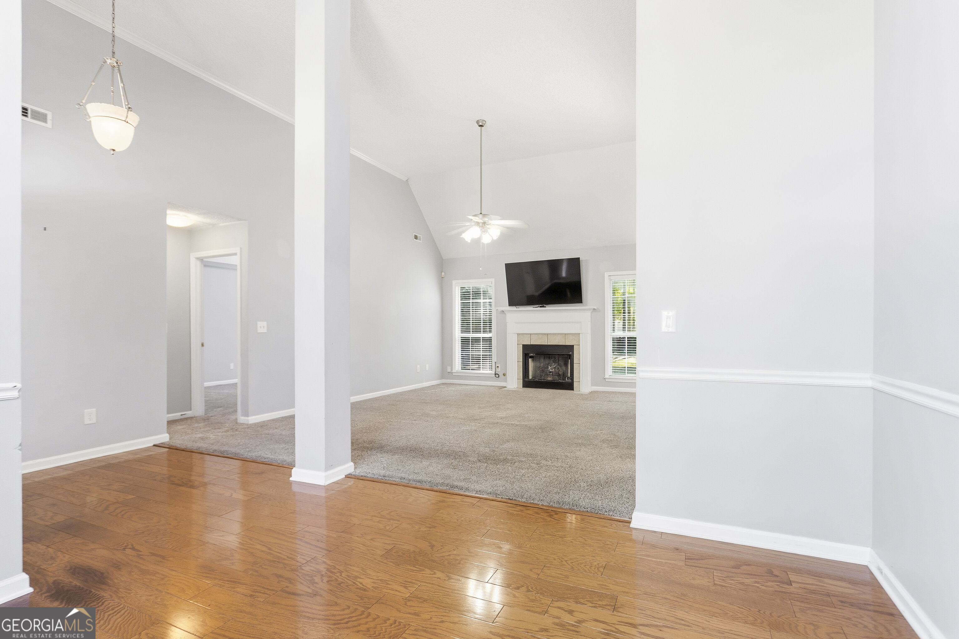 Vacant living room with a vaulted ceiling, fireplace, and television above the mantel.