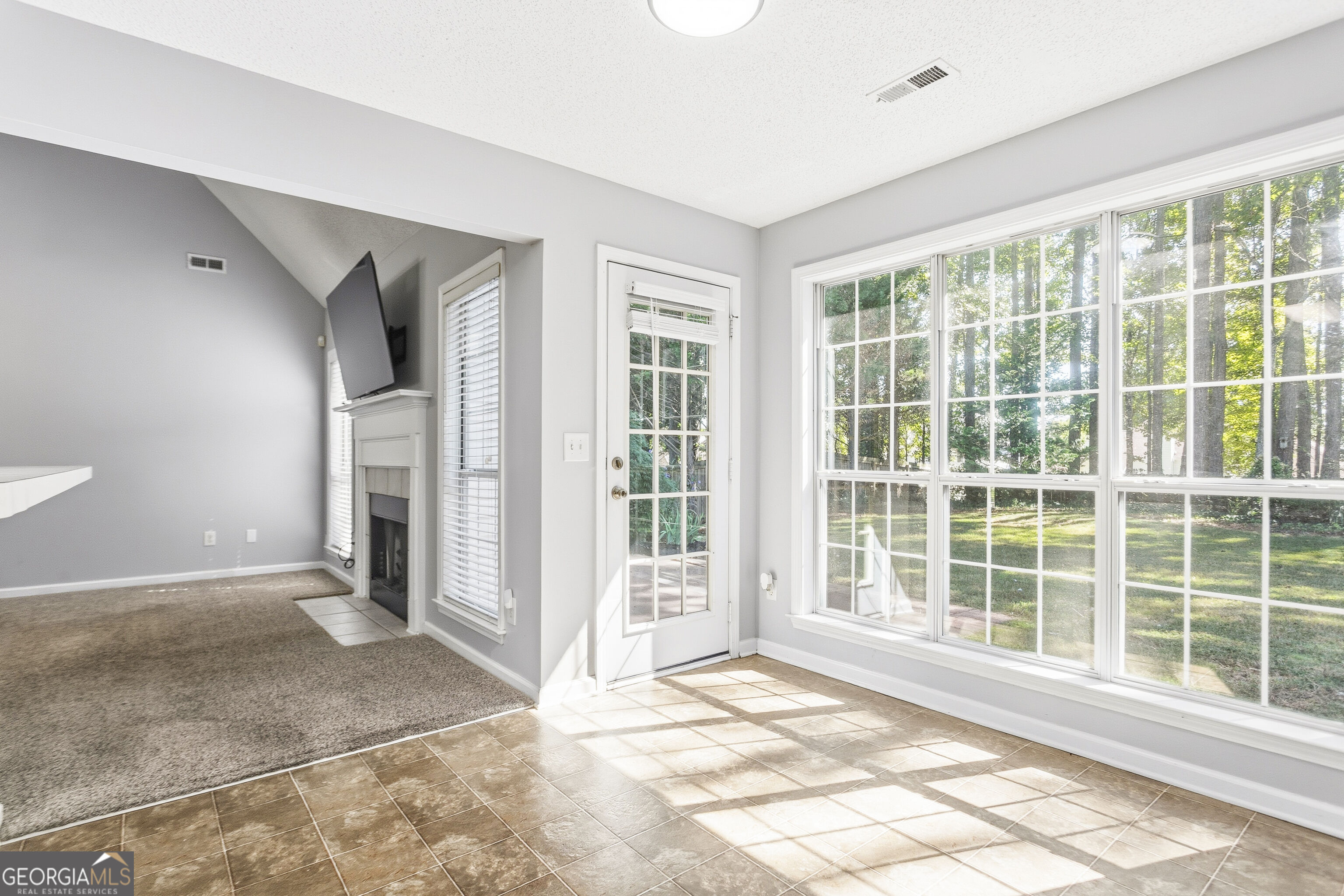 Sunroom with large windows, tiled flooring, and a view of the wooded yard.