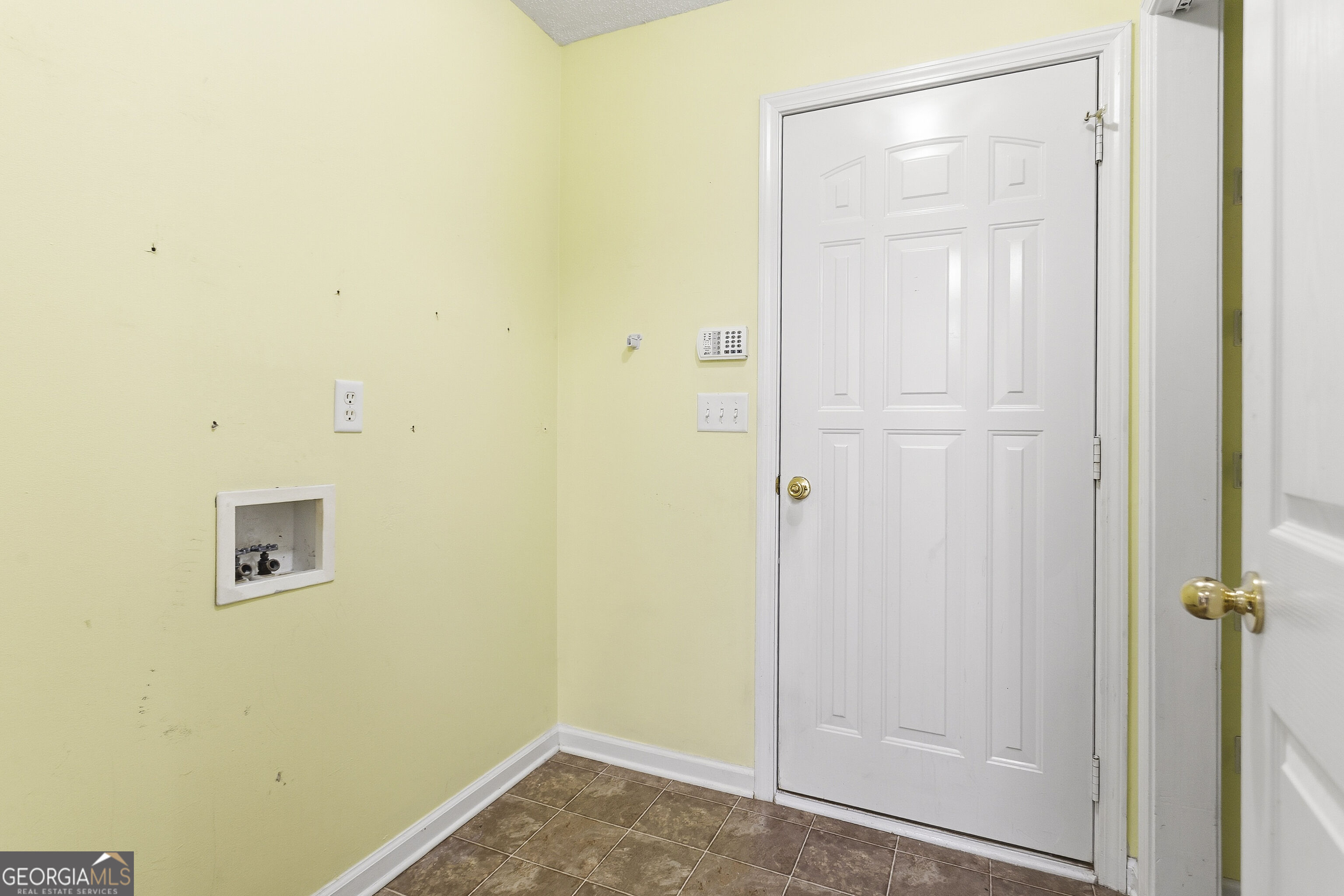 Empty laundry area with washer hookups, brown tile flooring, and a white paneled door.