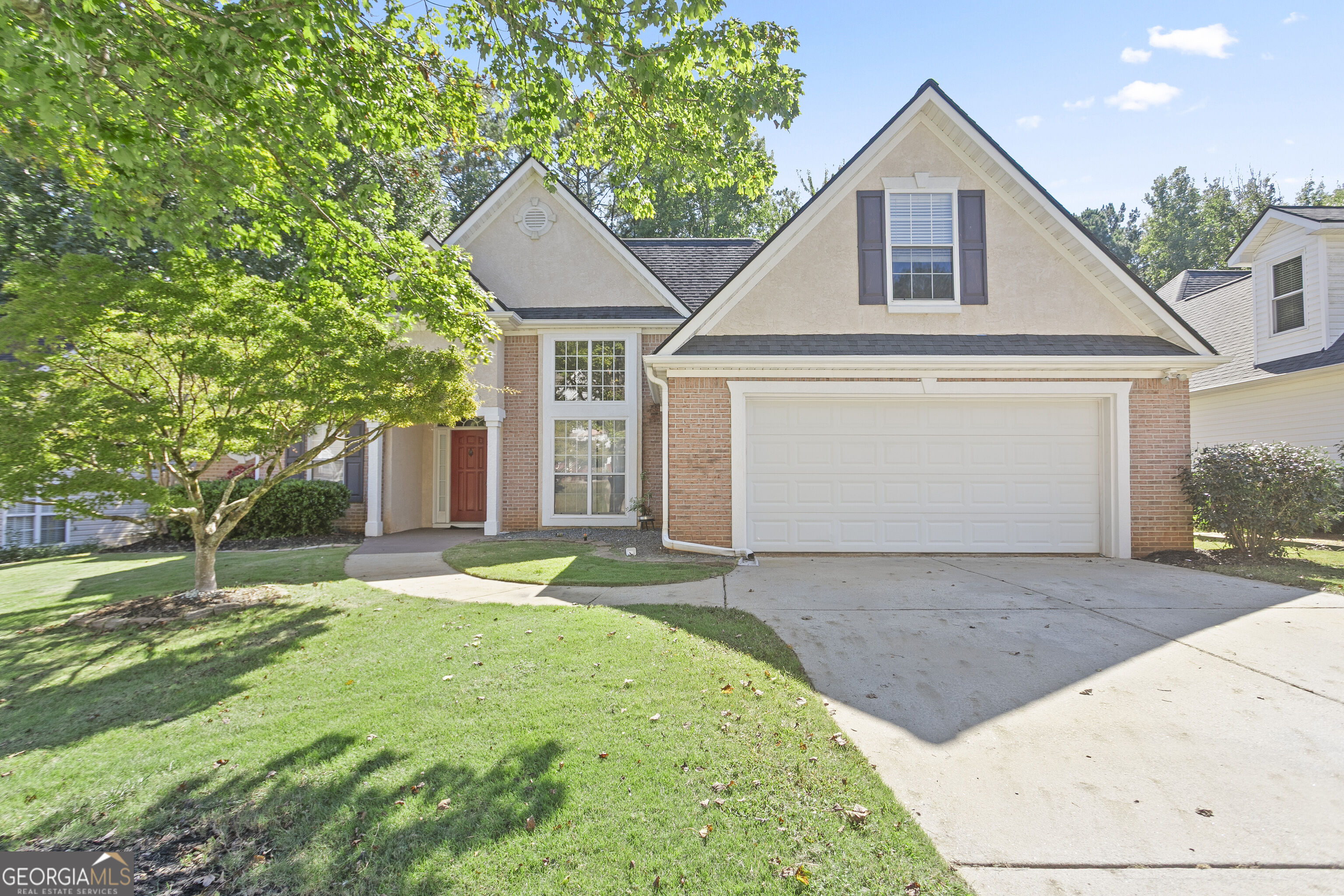 Two-story brick and stucco home with steep gables, a double garage, and a mature tree shading the front lawn.