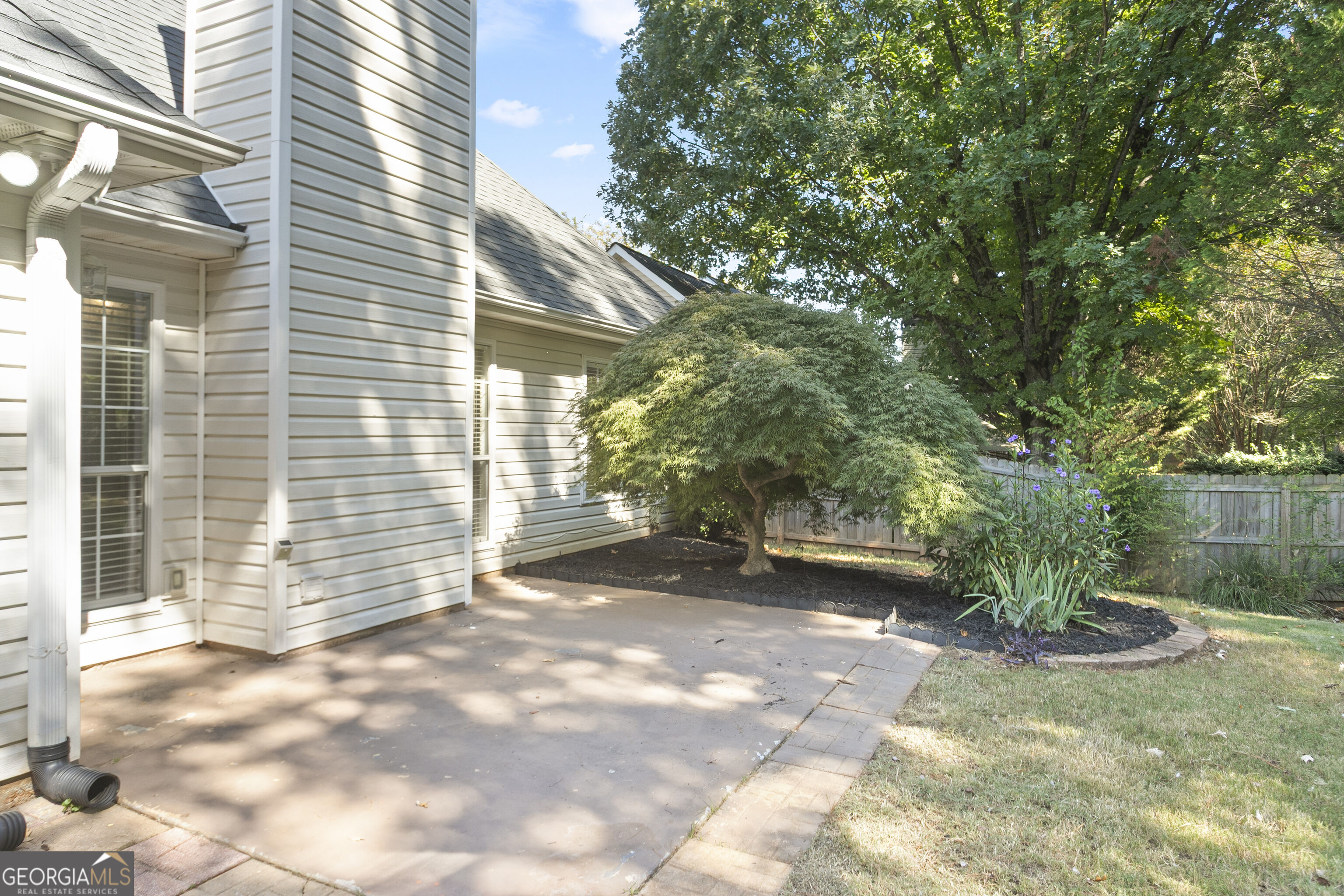 Home’s backyard patio beside a mature Japanese maple and landscaped flower beds.