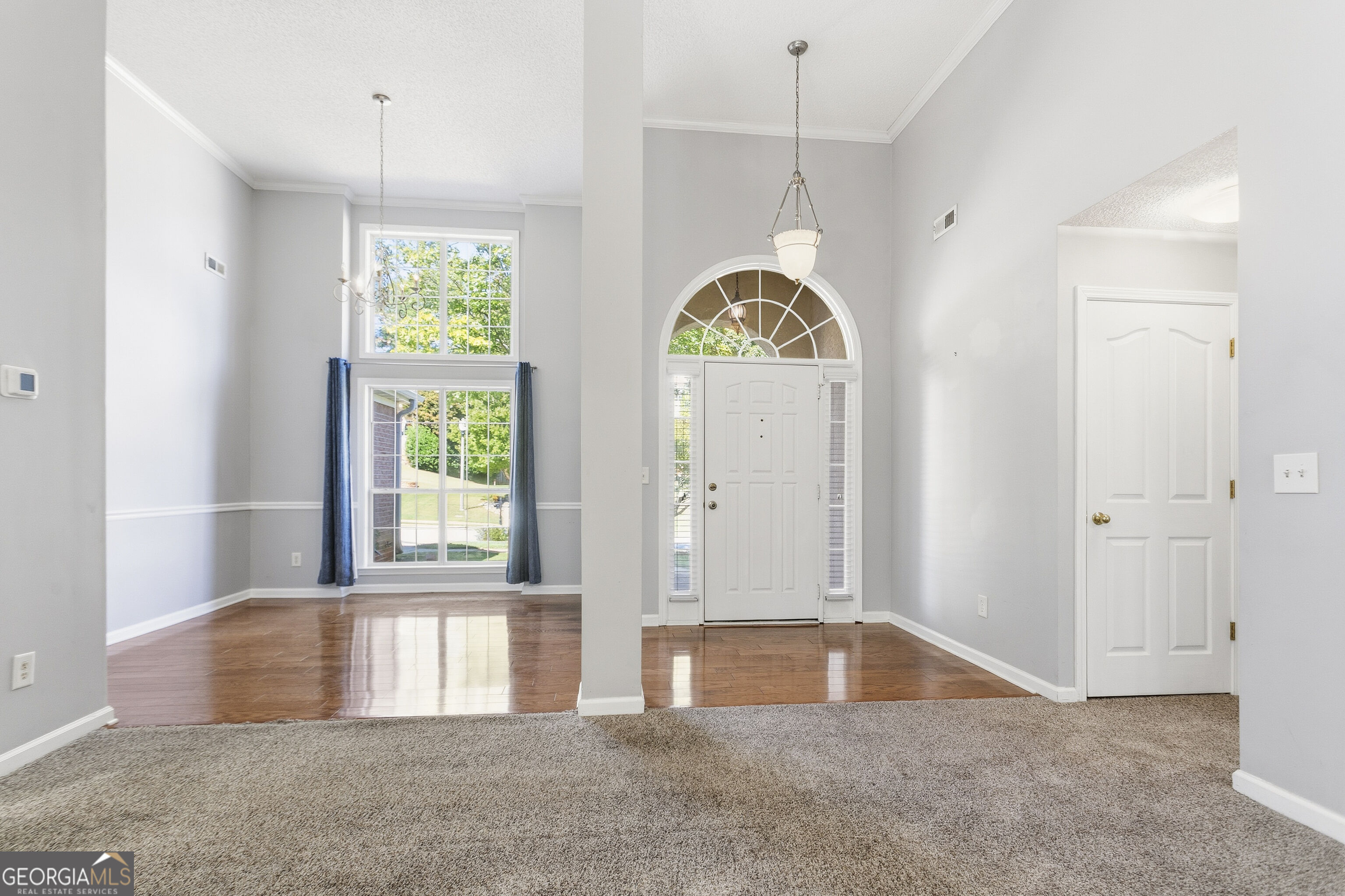Empty entry foyer with an arched front-door window, chandelier, and tall curtained windows.