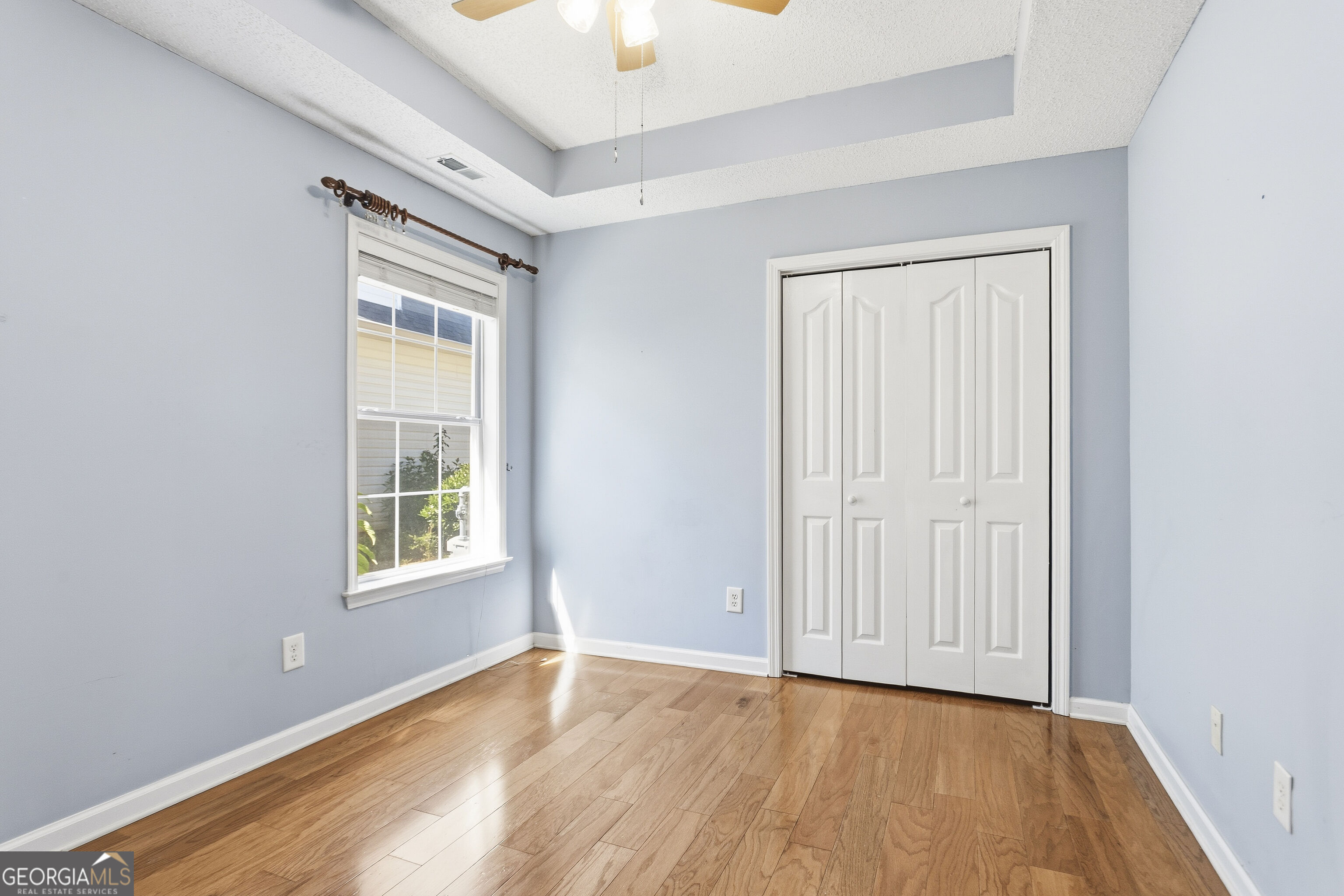 Empty bedroom with hardwood floors, pale blue walls, and white double closet doors.
