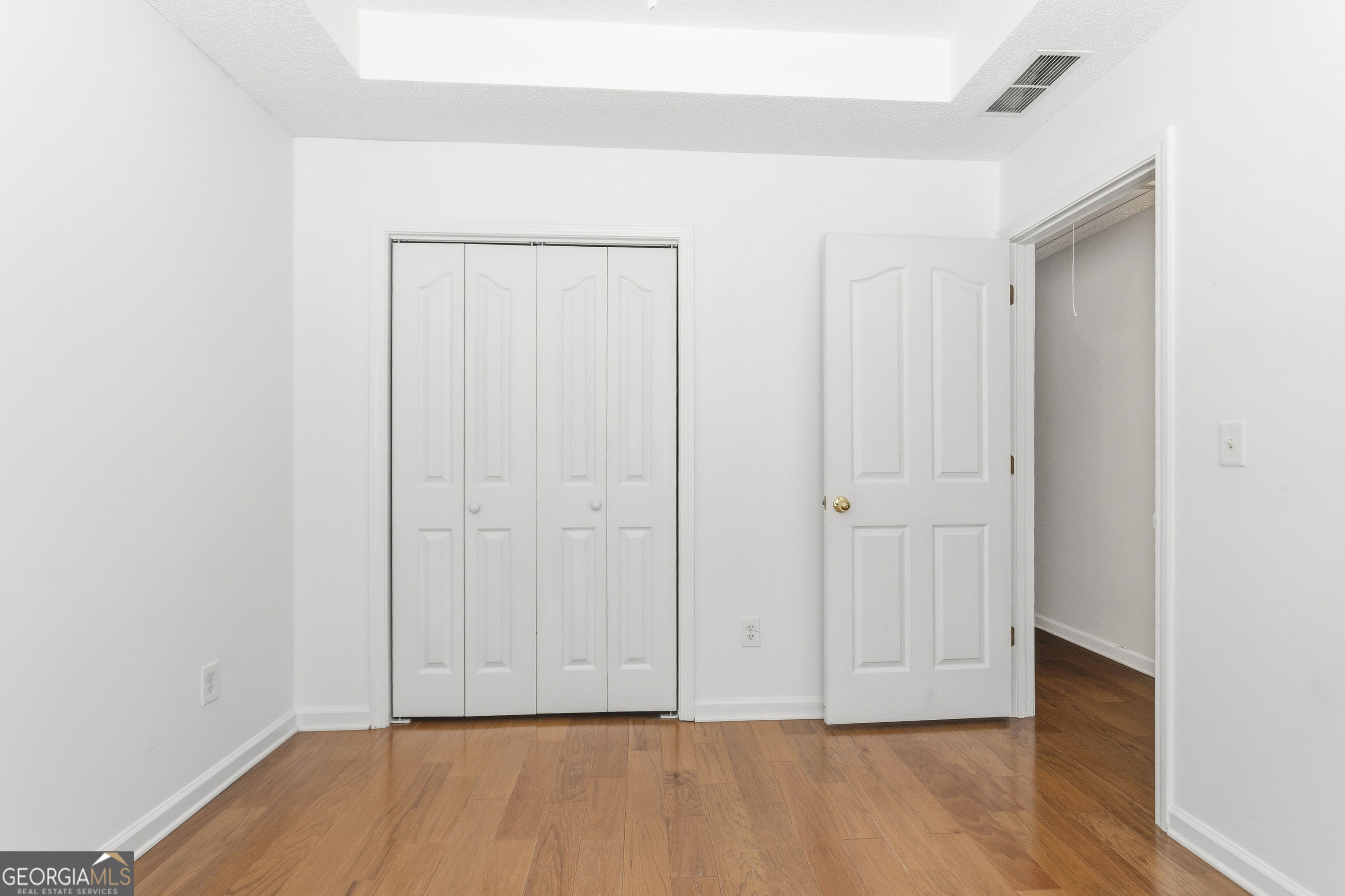 Empty bedroom with a four-panel closet, open doorway, and hardwood floors.