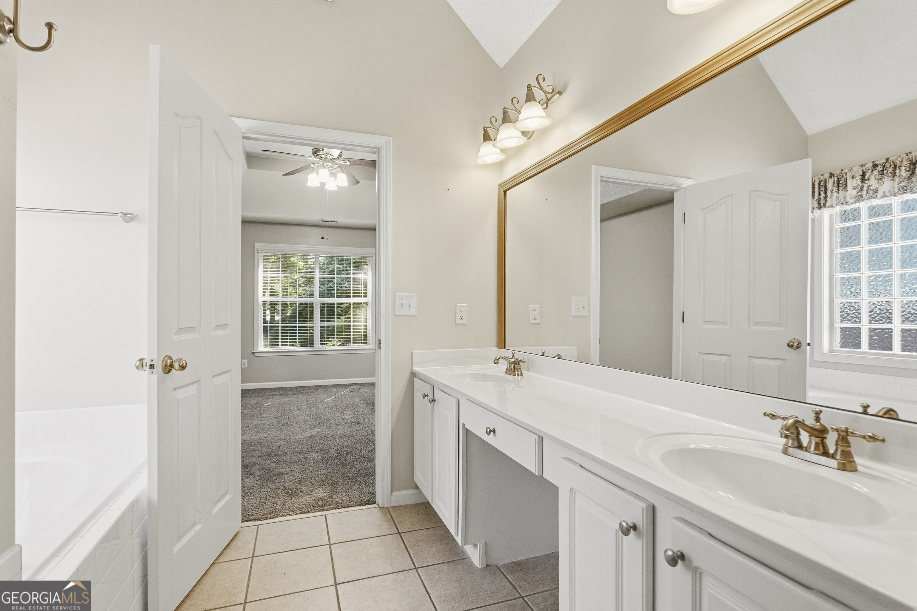 Bathroom with a long white double-sink vanity, brass faucets, and a large framed mirror.