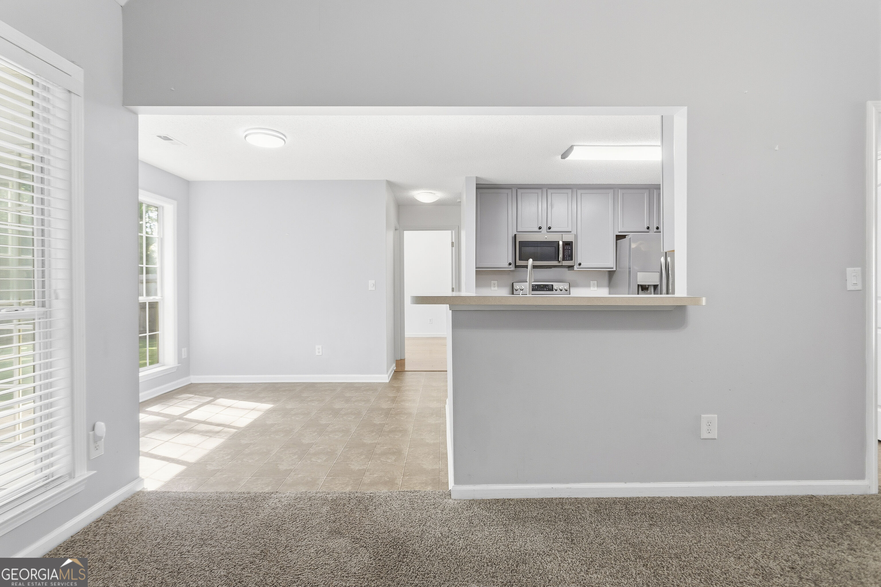Open kitchen with gray cabinets, stainless steel appliances, and a breakfast bar beside a sunlit tiled dining area.
