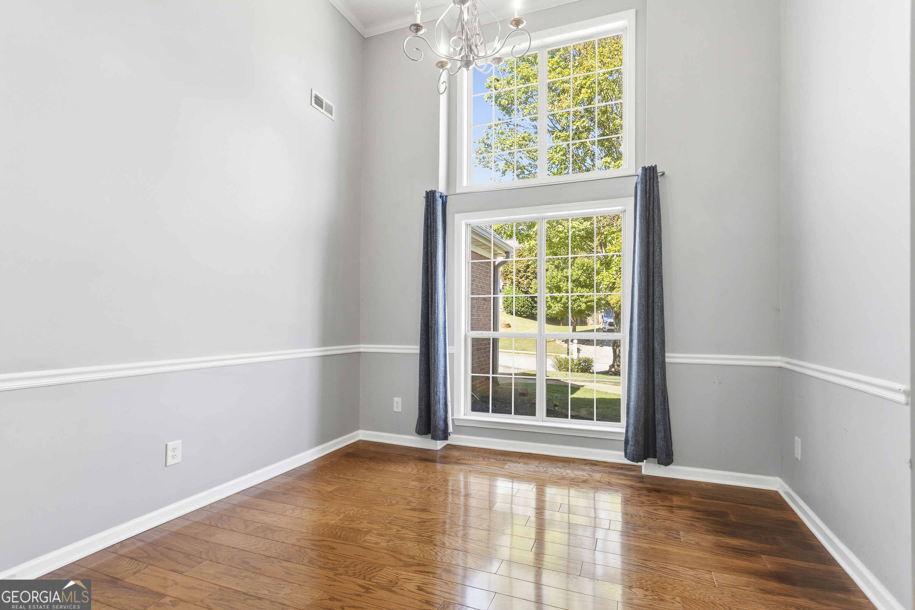 Empty dining room with polished hardwood floors, a chandelier, and tall paired windows.