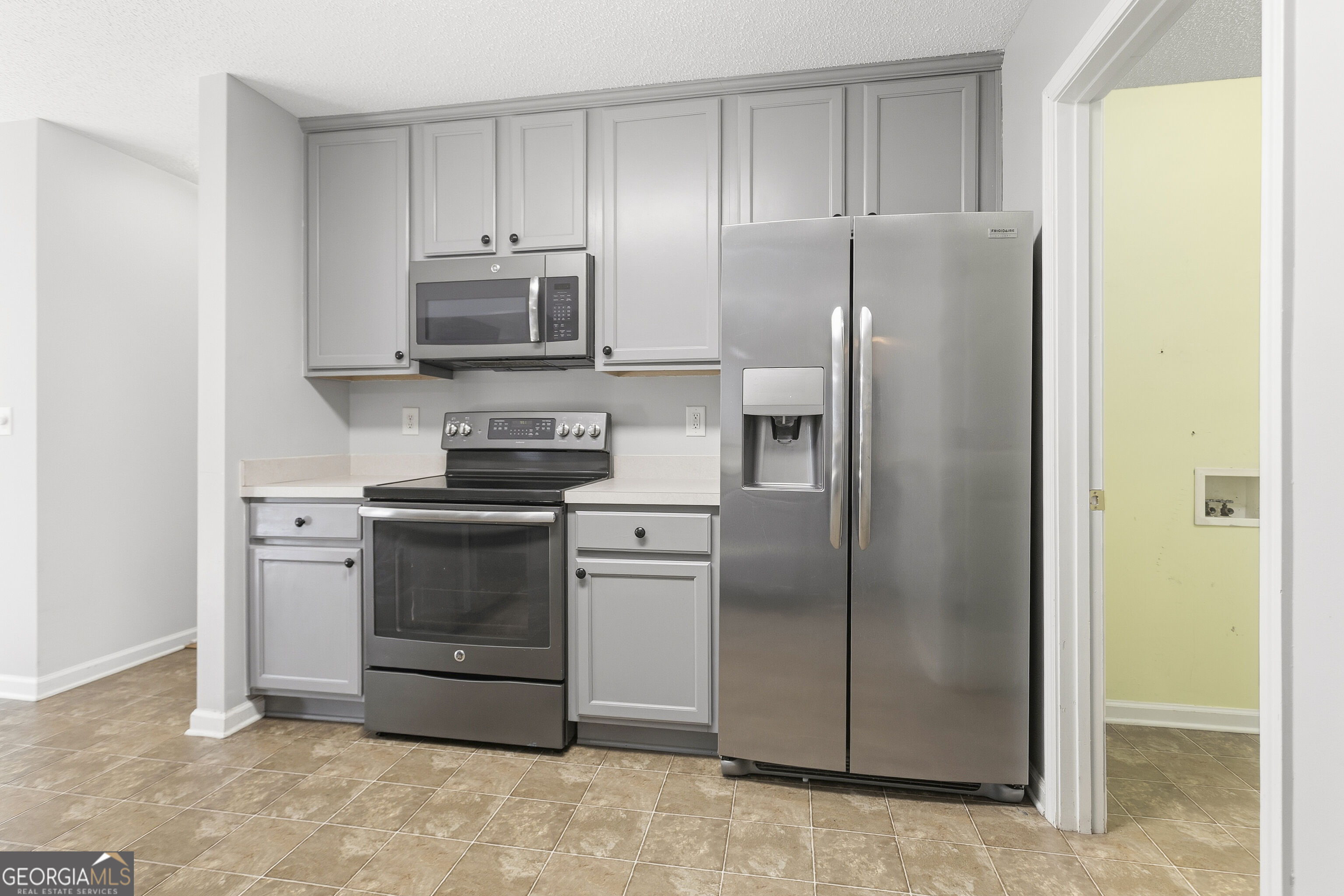 Kitchen with gray cabinets, stainless steel appliances, and tan tile flooring.