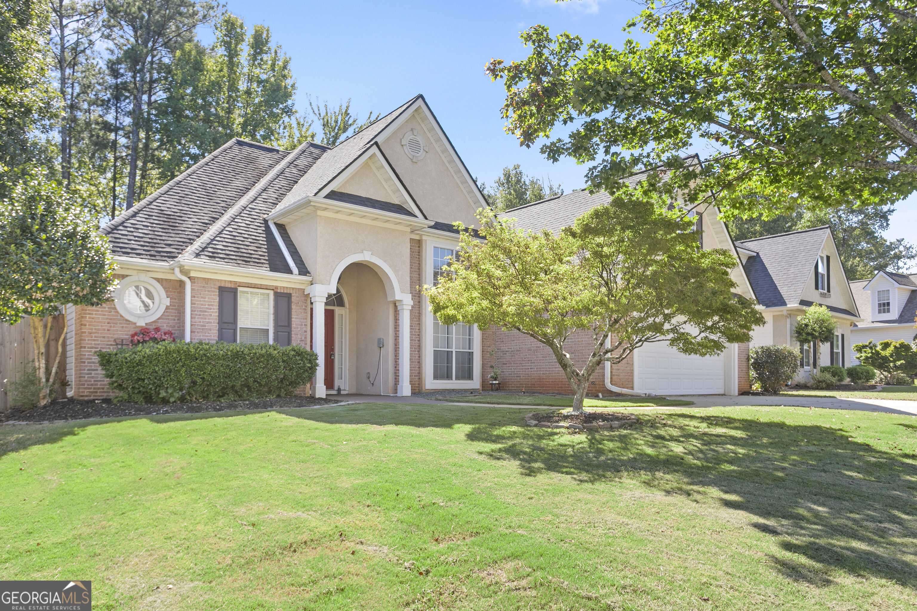 Two-story brick and stucco home with an arched entry, attached garage, and shaded front lawn.