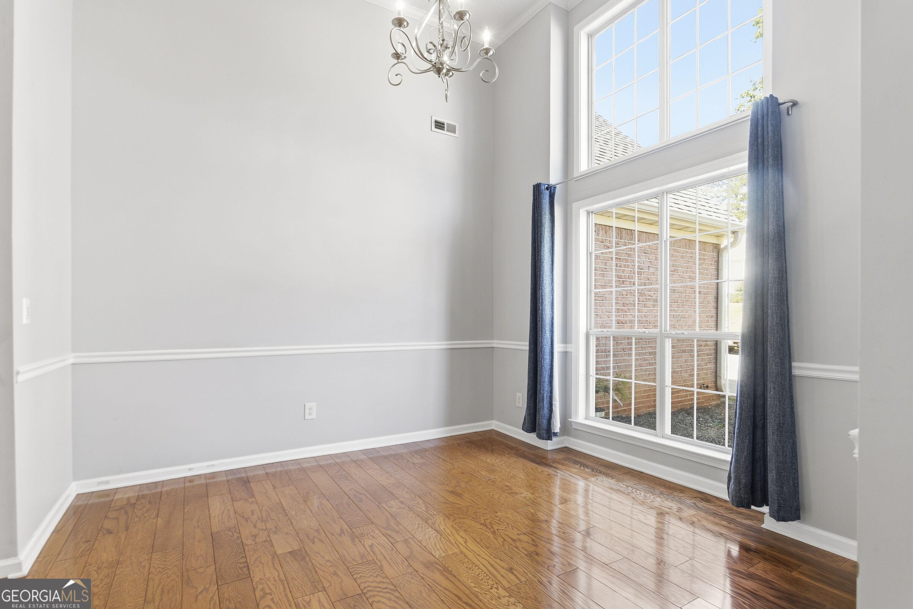 Unfurnished room with polished hardwood floors, a chandelier, and tall windows with blue curtains.