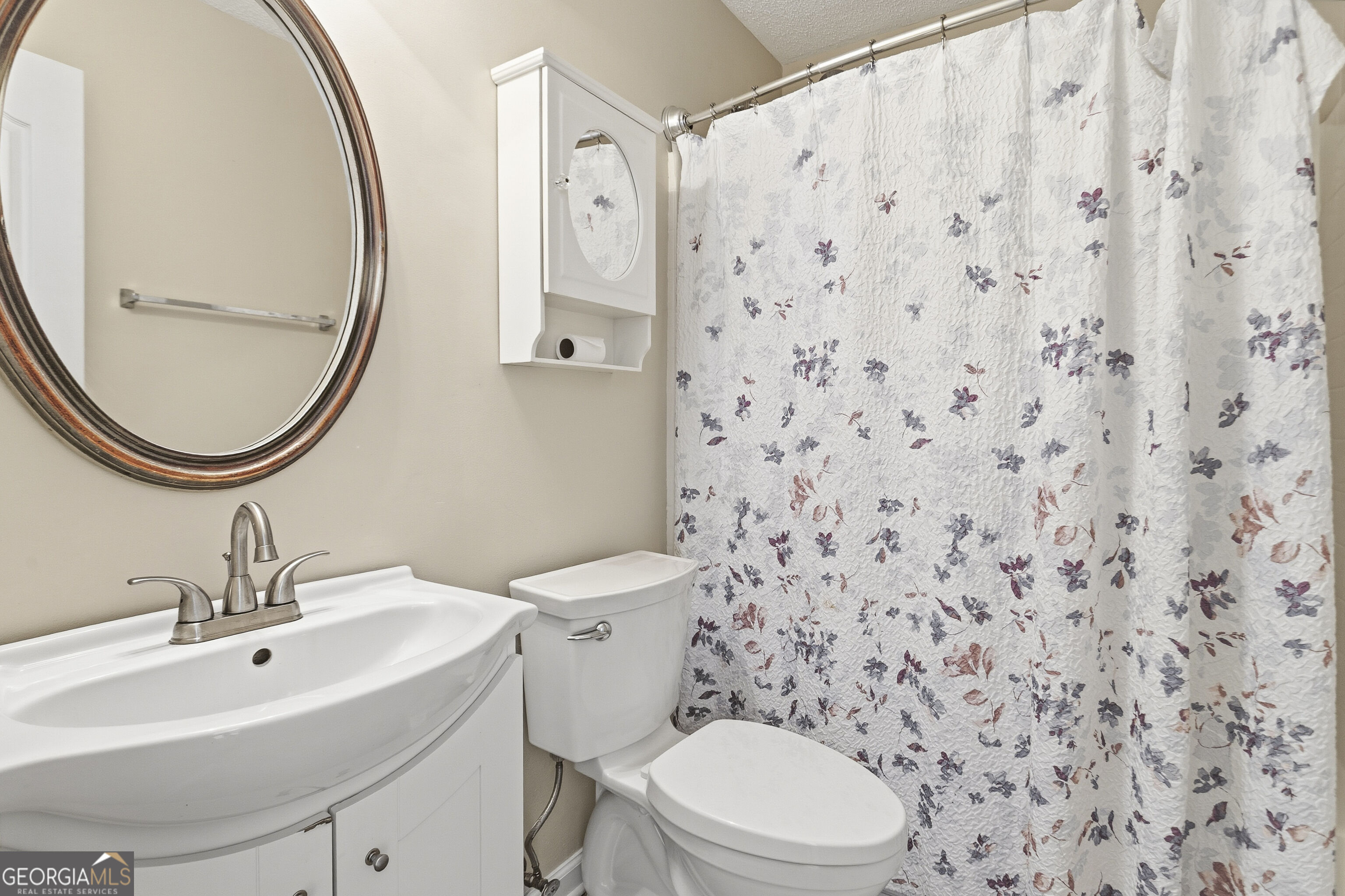 Bathroom with a white vanity, oval mirror, toilet, and floral shower curtain.