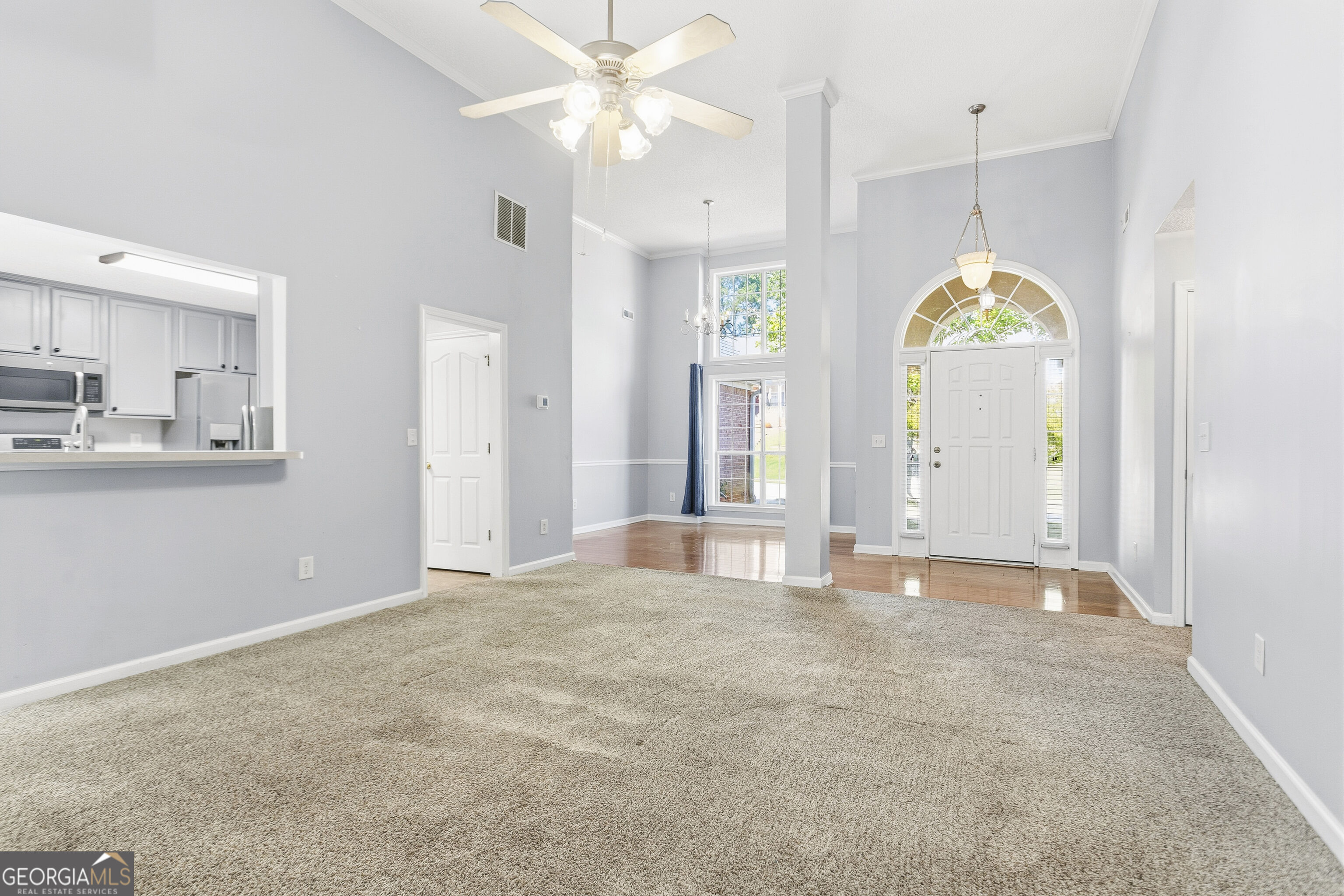 Vacant living room with beige carpet, open kitchen, and arched window above the front door.