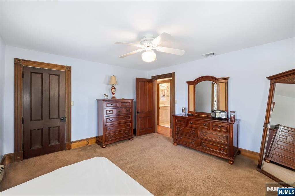 Bedroom with dark wood dressers, beige carpet, and an open doorway to the bathroom.