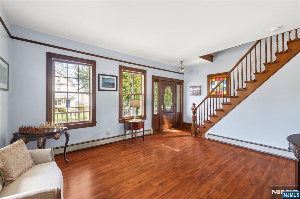 Living room with hardwood floors, large windows, and a wooden staircase beside the front door.