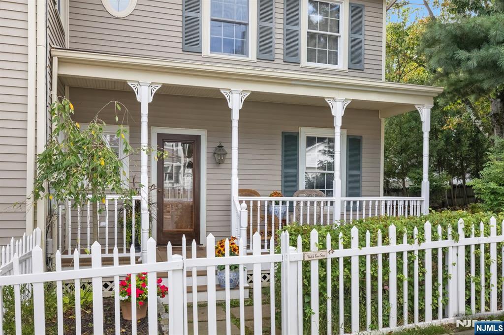 Home exterior with a covered porch, white picket fence, and flowering garden.