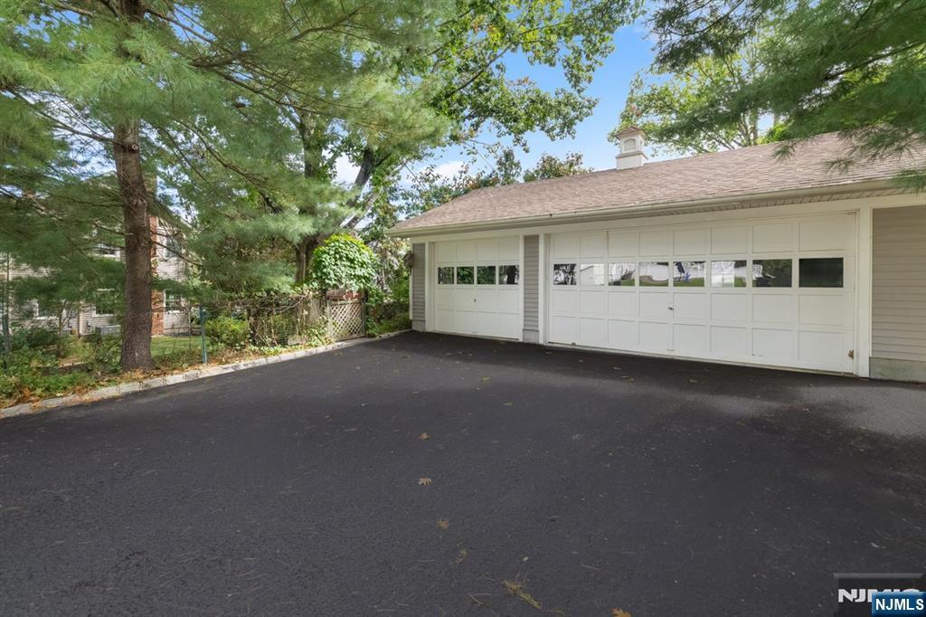 White two-door garage and broad asphalt driveway beneath mature trees.