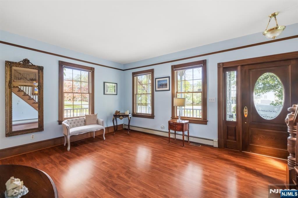 Entry foyer with polished hardwood floors, tall windows, and a dark wood front door with oval glass.