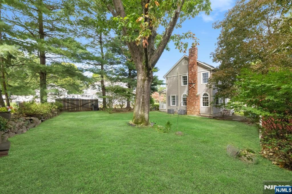 Rear of a two-story house with a brick chimney, a broad lawn, and mature trees.