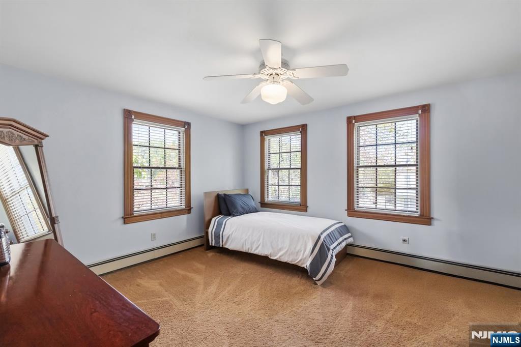 Bedroom with a single bed, beige carpet, and three wood-trimmed windows.