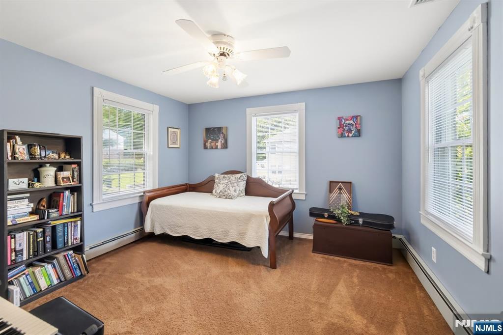 Bedroom with a wooden bed, blue walls, tan carpet, and bookshelves beneath several windows.