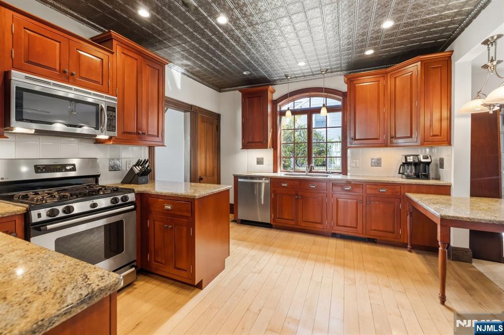 Kitchen with reddish-brown cabinets, granite countertops, stainless steel appliances, and a patterned tin ceiling.