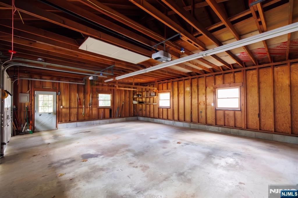 Empty garage with exposed wooden framing, concrete floor, and windows.