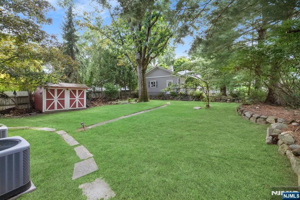 Backyard with a broad lawn, stepping-stone path, red shed, mature trees, and stone borders.