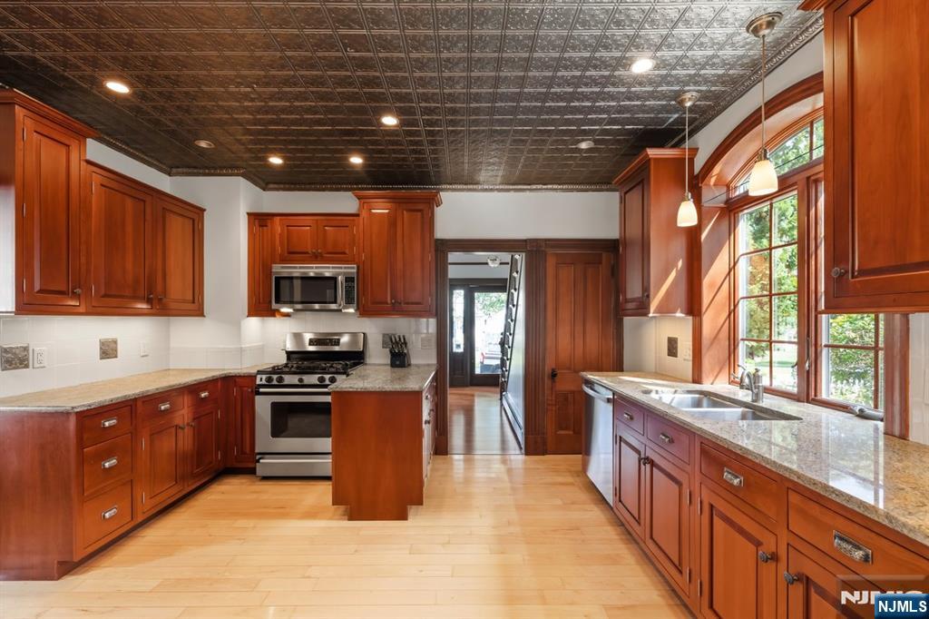 Kitchen with reddish wood cabinetry, granite counters, and large arched windows beside the sink.