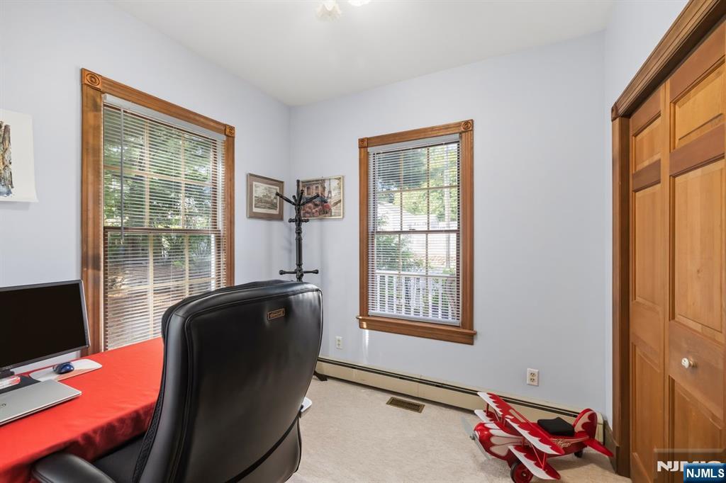 Furnished home office with two wood-trimmed windows, a red desk, and a model airplane.