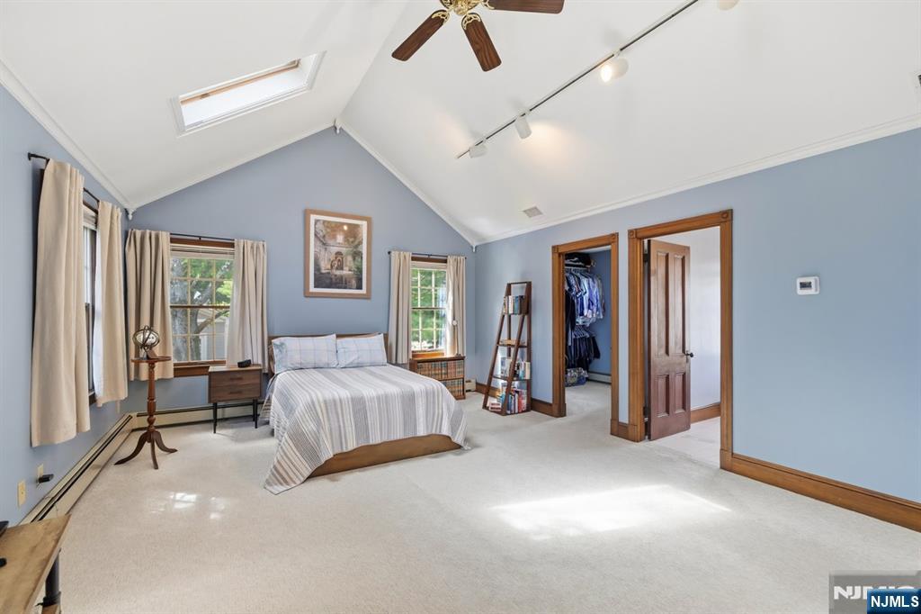 Furnished bedroom with a vaulted ceiling, skylight, pale blue walls and wood-trimmed doorways.