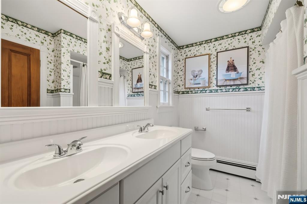 Bathroom with a long double-sink vanity, floral wallpaper, beadboard wainscoting, and framed animal prints.