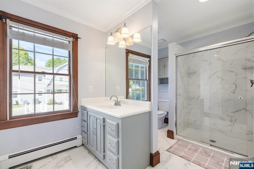 Bathroom with a gray vanity, wood-trimmed window, and glass-enclosed marble-look shower.