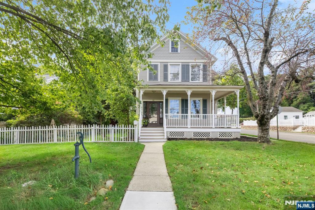 Two-story house with a covered porch, white picket fence, and walkway through the front lawn.