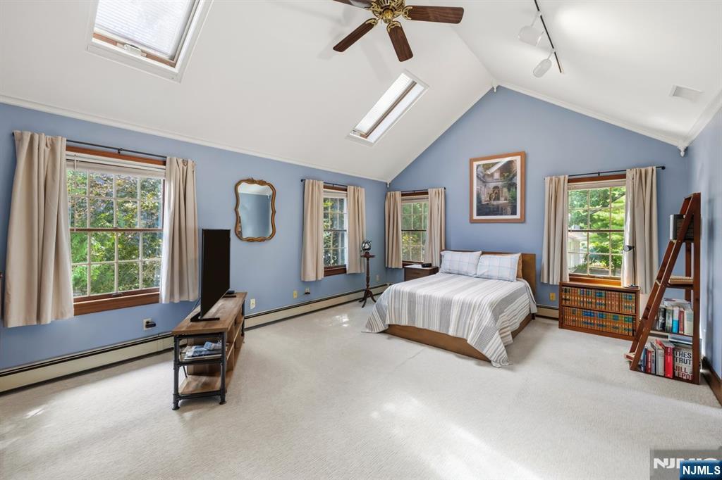 Furnished bedroom with vaulted ceiling, skylights, blue walls, and a bed between curtained windows.